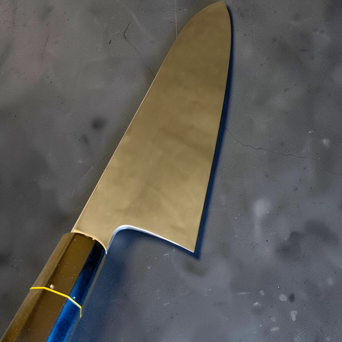 Close-up of the Nakagawa honyaki blade, polished choil and heel beside the gold-colored Prisma handle spacer