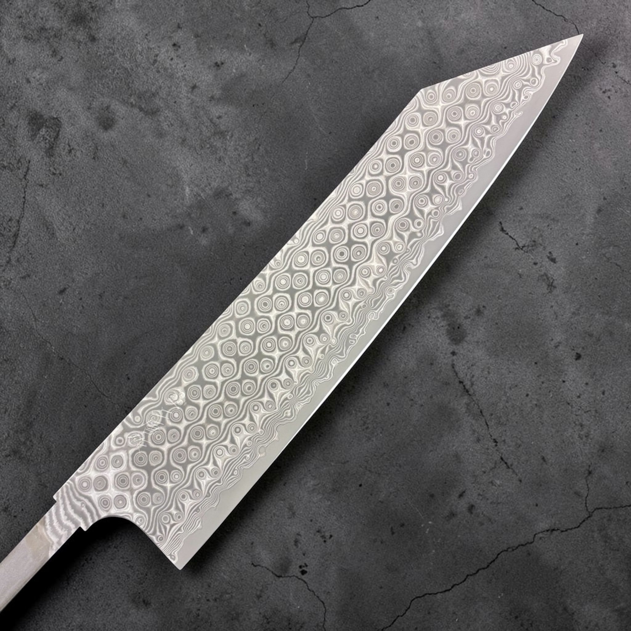 Nigara Anmon SG2 Kiritsuke Gyuto 240 mm, close-up of the Damascus Anmon pattern showing layered steel rings and wavy lines on a kiritsuke-style blade. Right side of the blade.