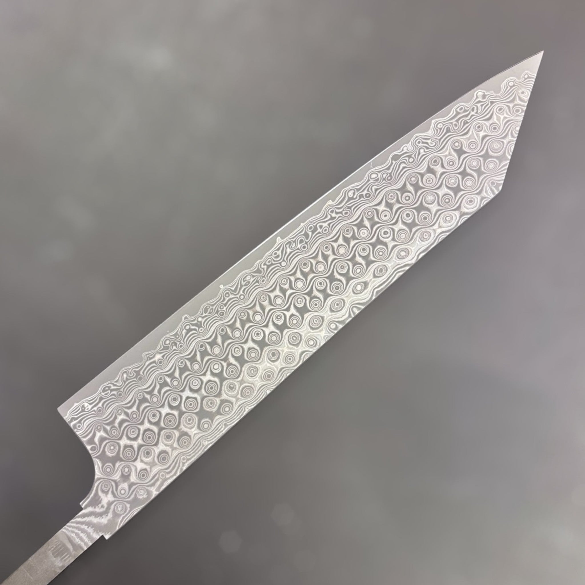 Nigara Anmon SG2 Kiritsuke Gyuto 240 mm, close-up of the Damascus Anmon pattern showing layered steel rings and wavy lines on a kiritsuke-style blade. Left side of blade.