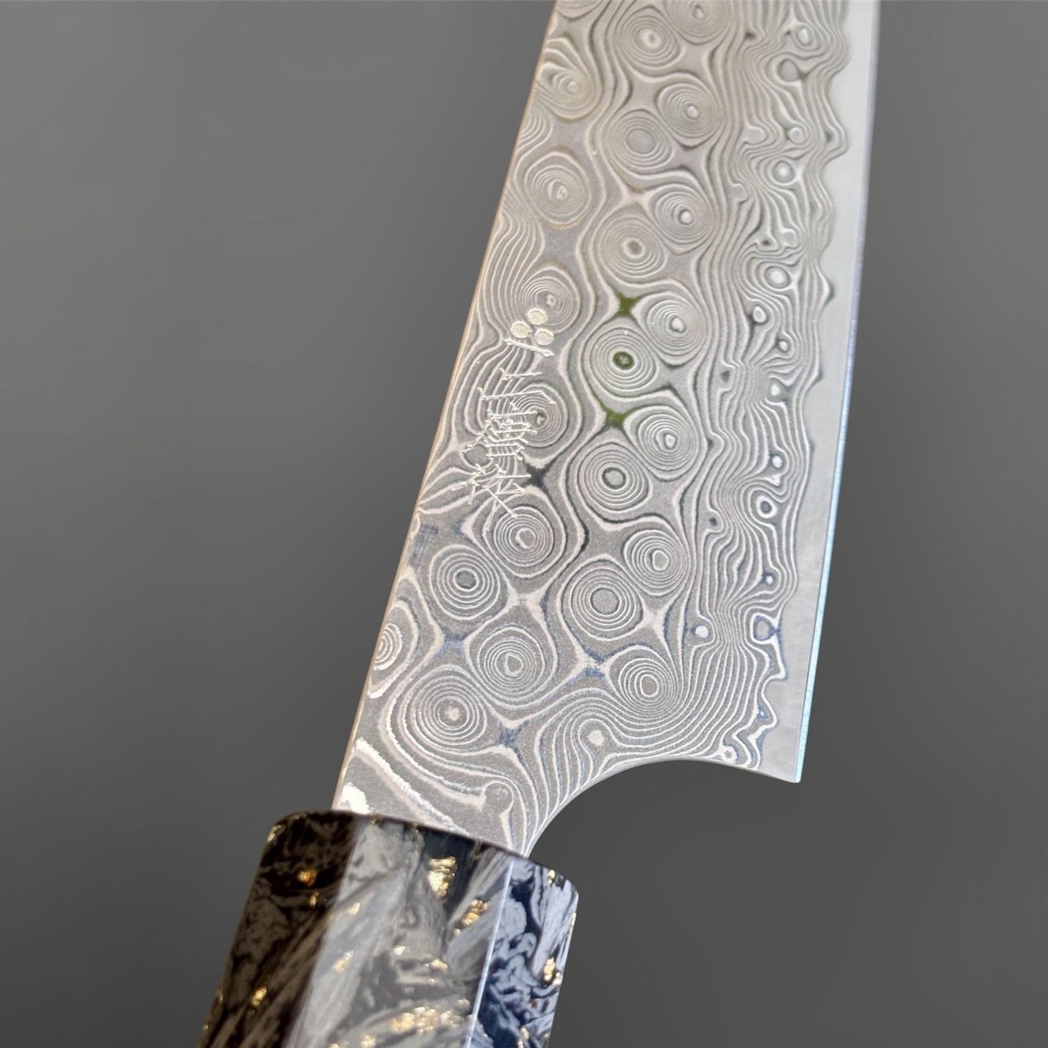 Nigara Anmon SG2 Petty 150 mm with carbon fiber and gold fleck handle, close-up of the Anmon damascus pattern near the heel.