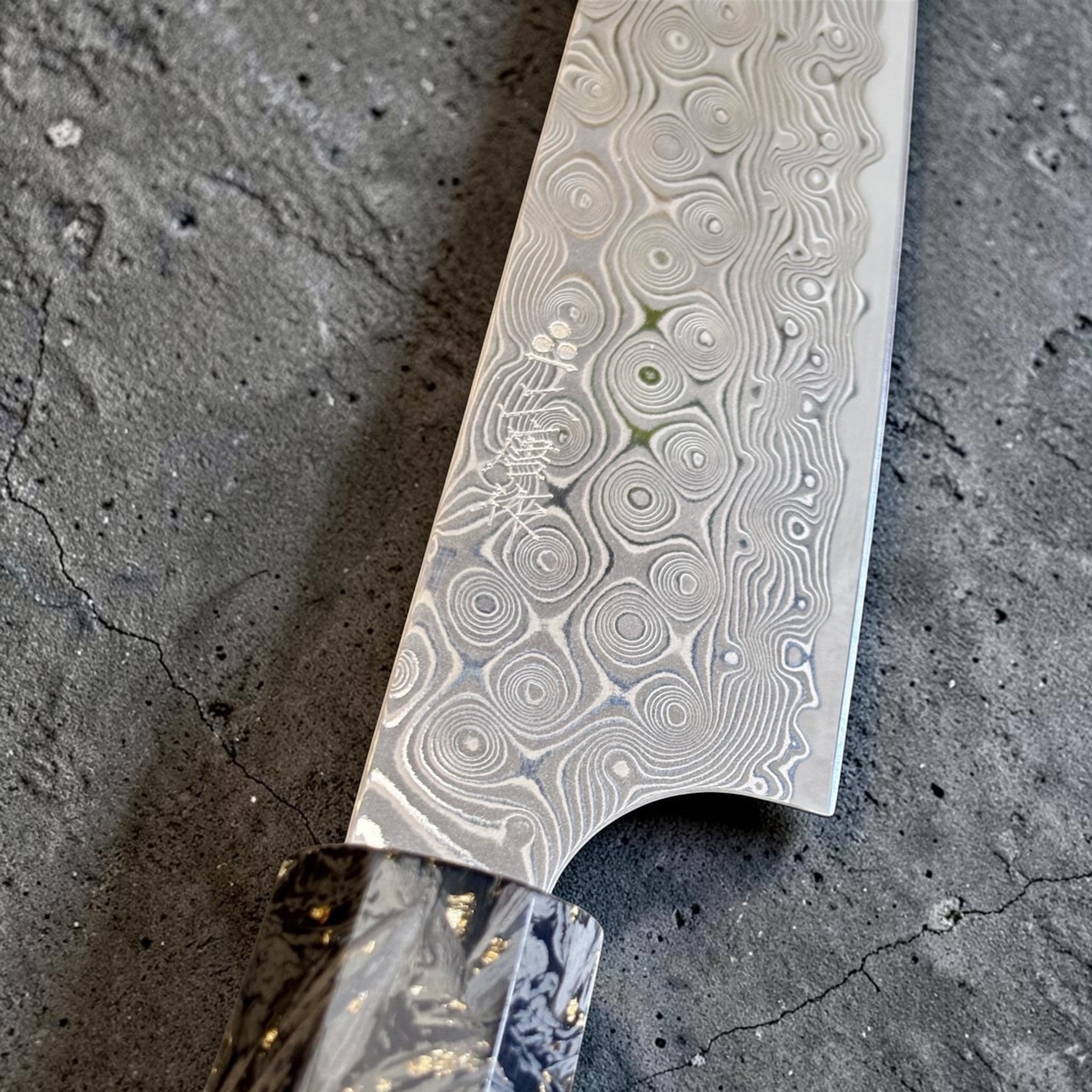 Nigara Anmon SG2 Petty 150 mm with carbon fiber and gold fleck handle, close-up of the Anmon damascus pattern near the heel.