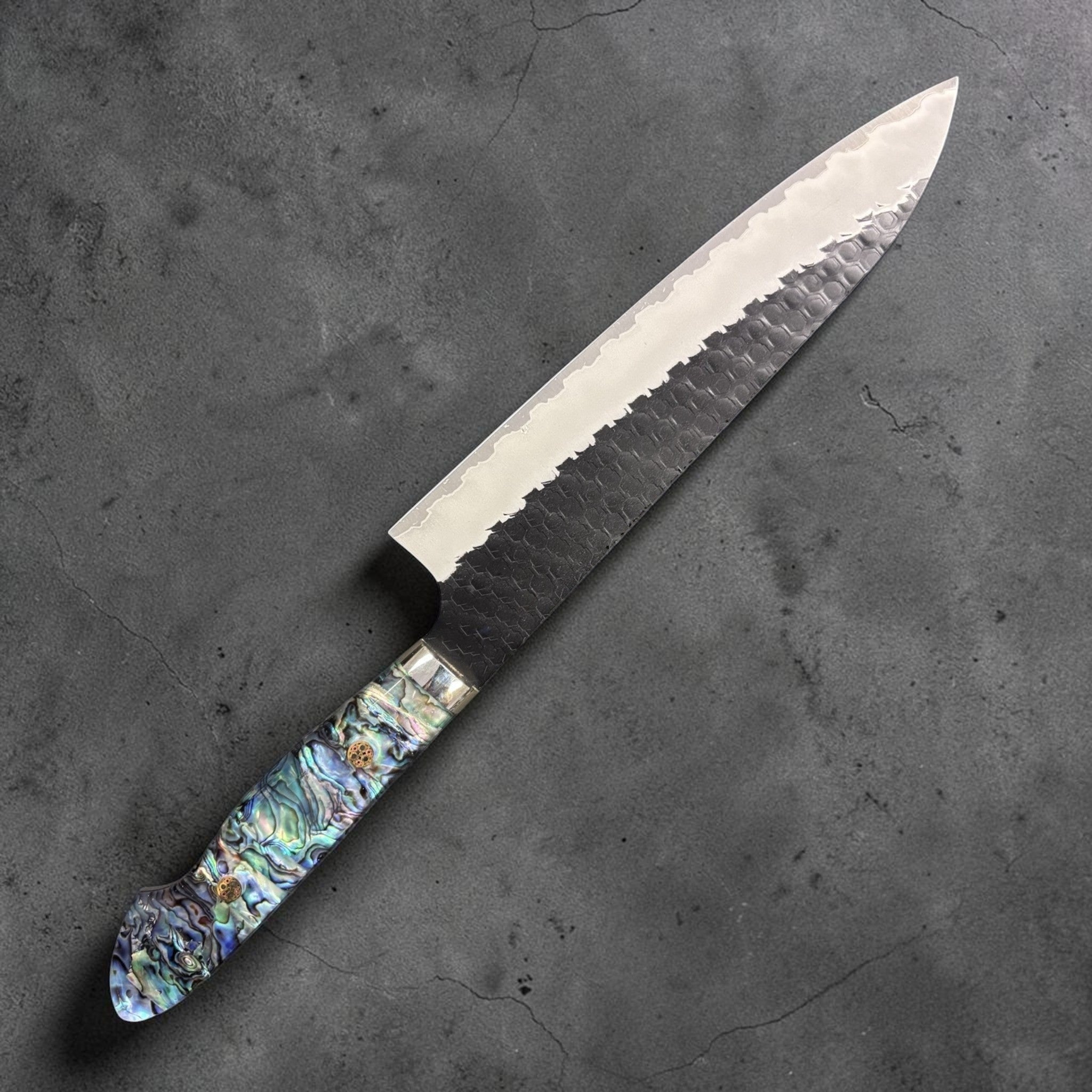 Nigara SG2 Kurouchi Tsuchime Gyuto 210 mm, left side profile highlighting the dark kurouchi cladding and iridescent handle.