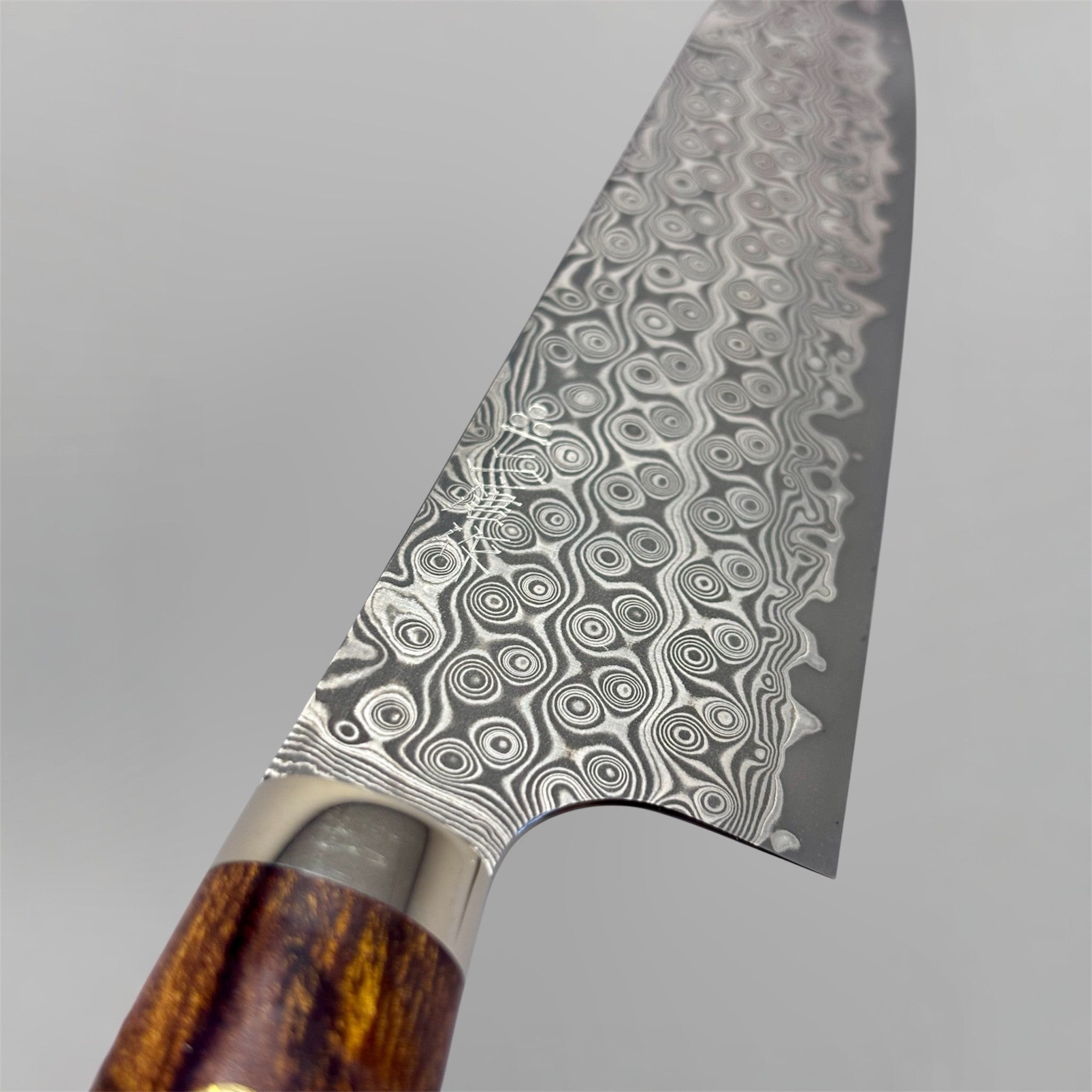 Nigara Hamono Anmon SG2 210 mm Gyuto with ironwood western handle, close-up of SG2 Anmon Damascus blade pattern near the heel.