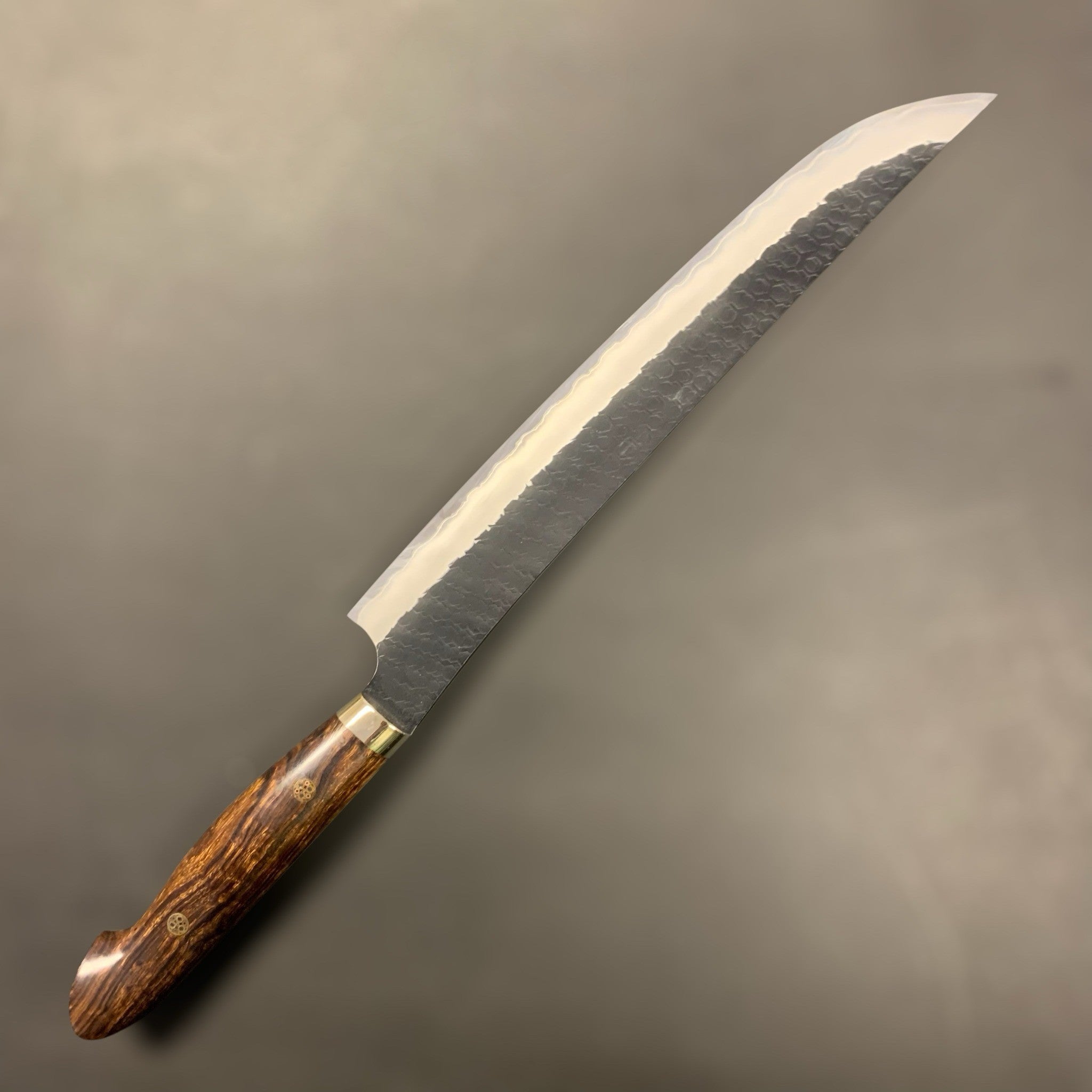 Nigara Hamono SG2 Kurouchi Tsuchime Sakimaru Sujihiki 270 mm, left-side profile highlighting the polished edge contrast against the dark kurouchi blade and ironwood Western handle.