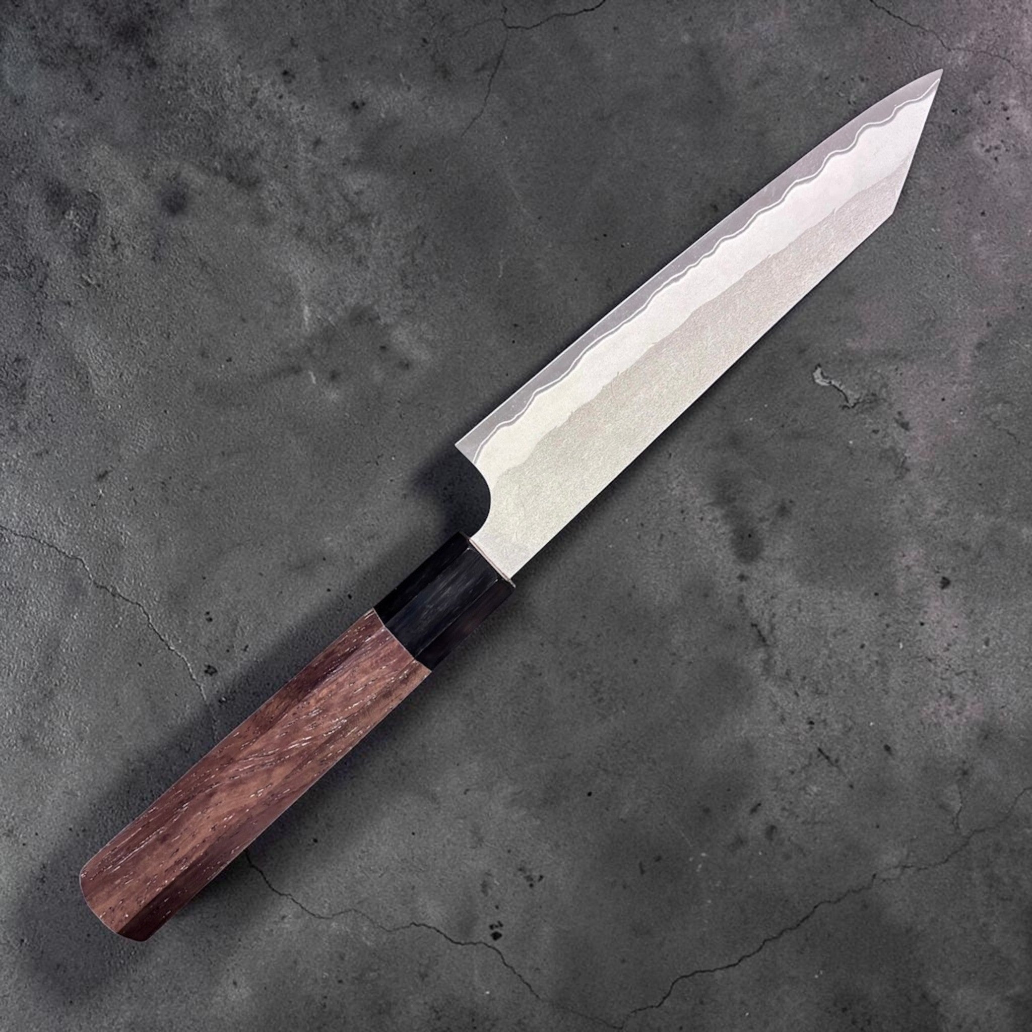 Nigara Hamono Aogami Super Tsuchime Kiritsuke Petty 150 mm with walnut handle, angled view, opposite side of blade on gray background.