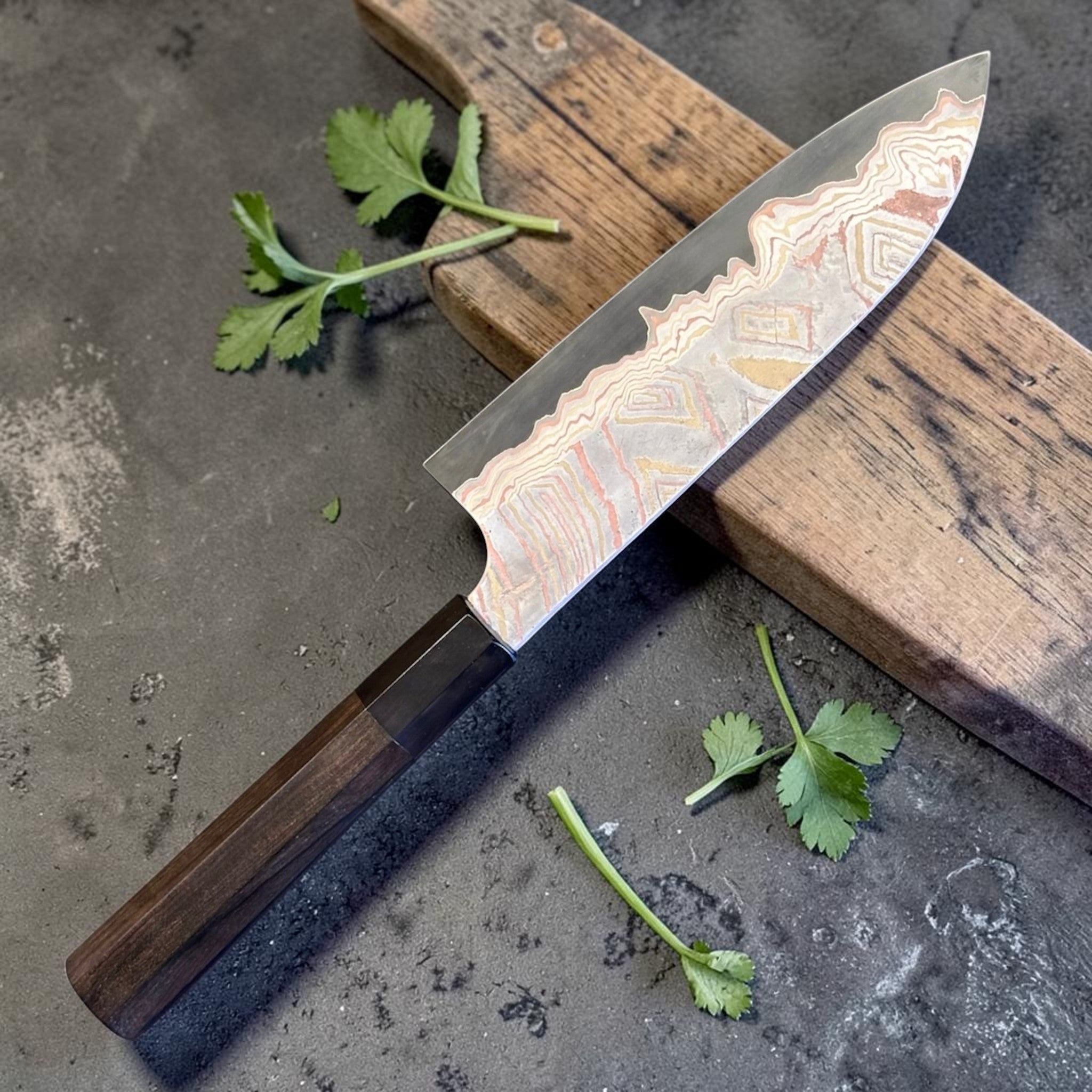 Nigara Irodori Blue #2 Rainbow Damascus Santoku 180 mm, alternate angled view emphasizing the polished core edge and dramatic layered damascus near the tip.