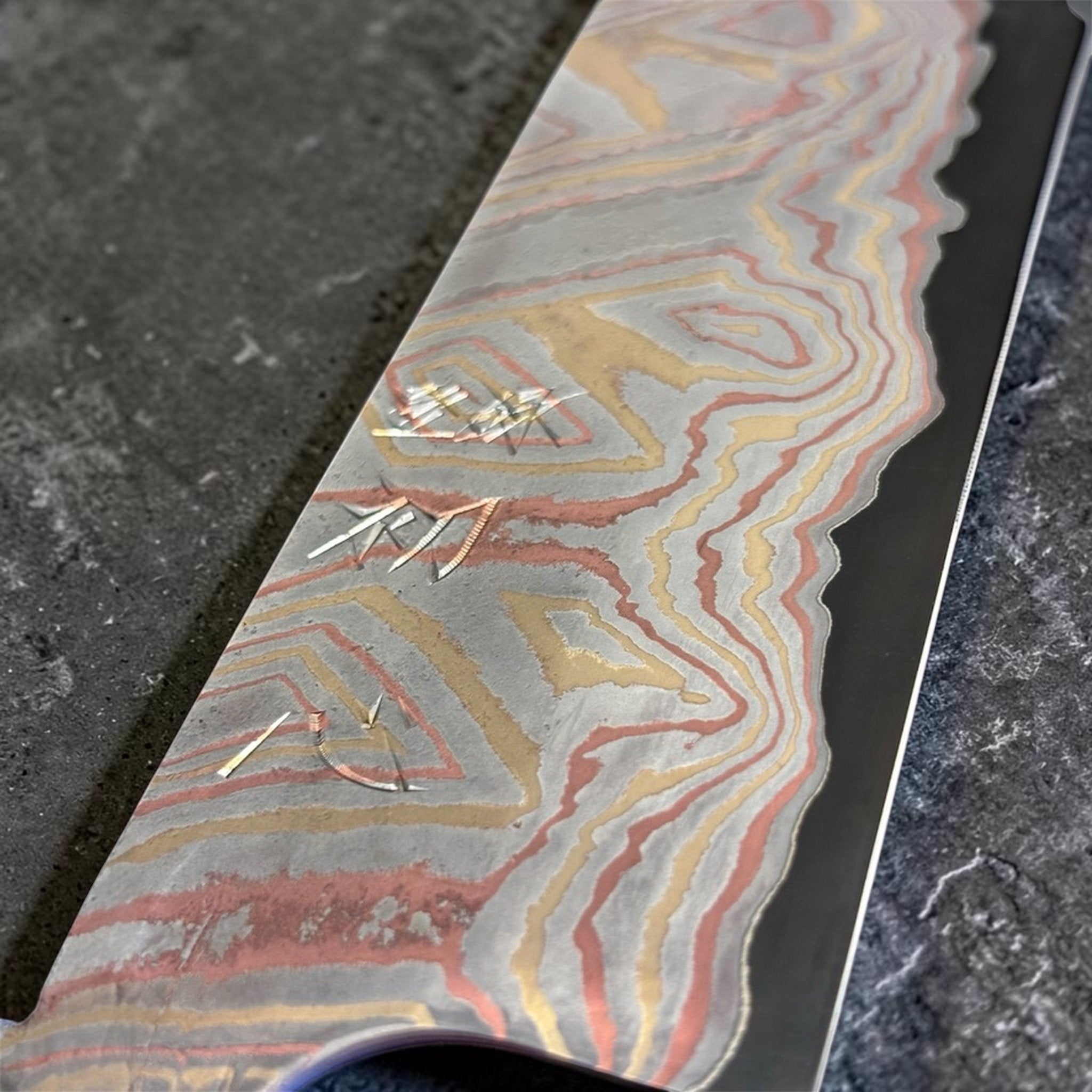 Close-up of the Nigara Irodori Blue #2 Rainbow Damascus Santoku 180 mm blade, showing the engraved kanji and intricate pink, gold, and silver damascus layers.