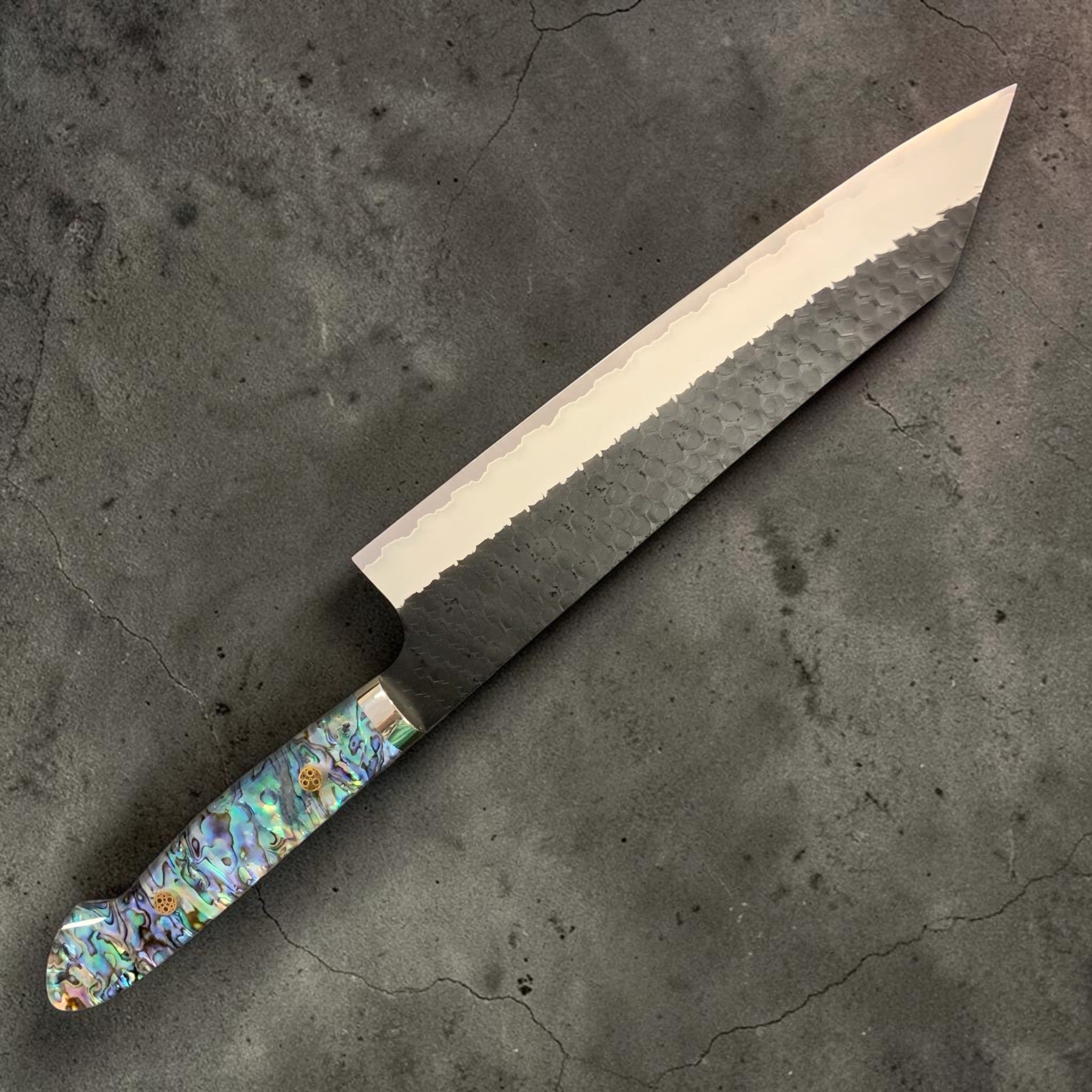 Nigara SG2 Kurouchi Tsuchime Kiritsuke 240 mm, left side profile showing hammered finish and abalone Western handle.