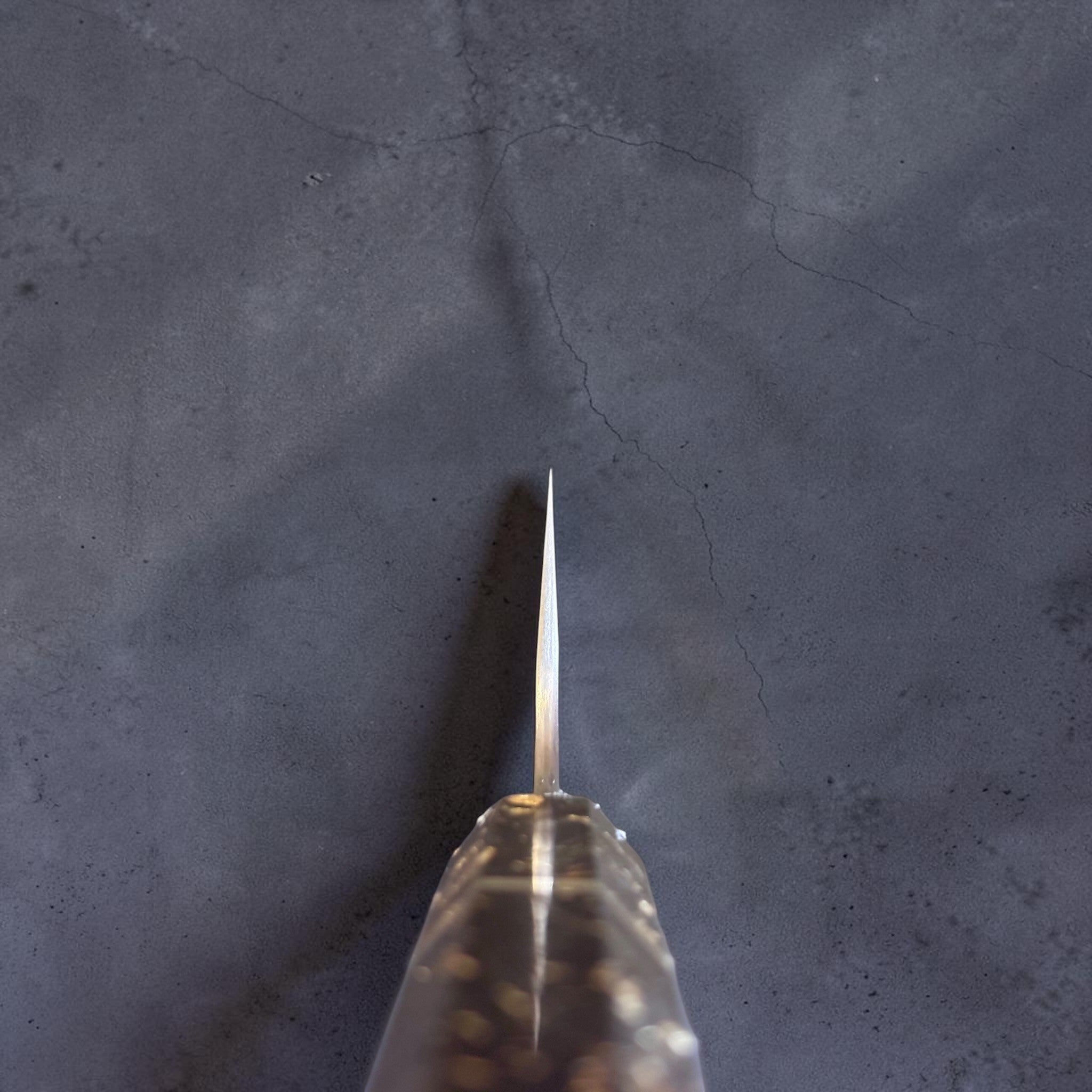Choil view of the Nigara SG-STRIX Ko Santoku 150 mm displaying the thin blade geometry, distal taper and custom carbon fiber and gold fleck wa handle.