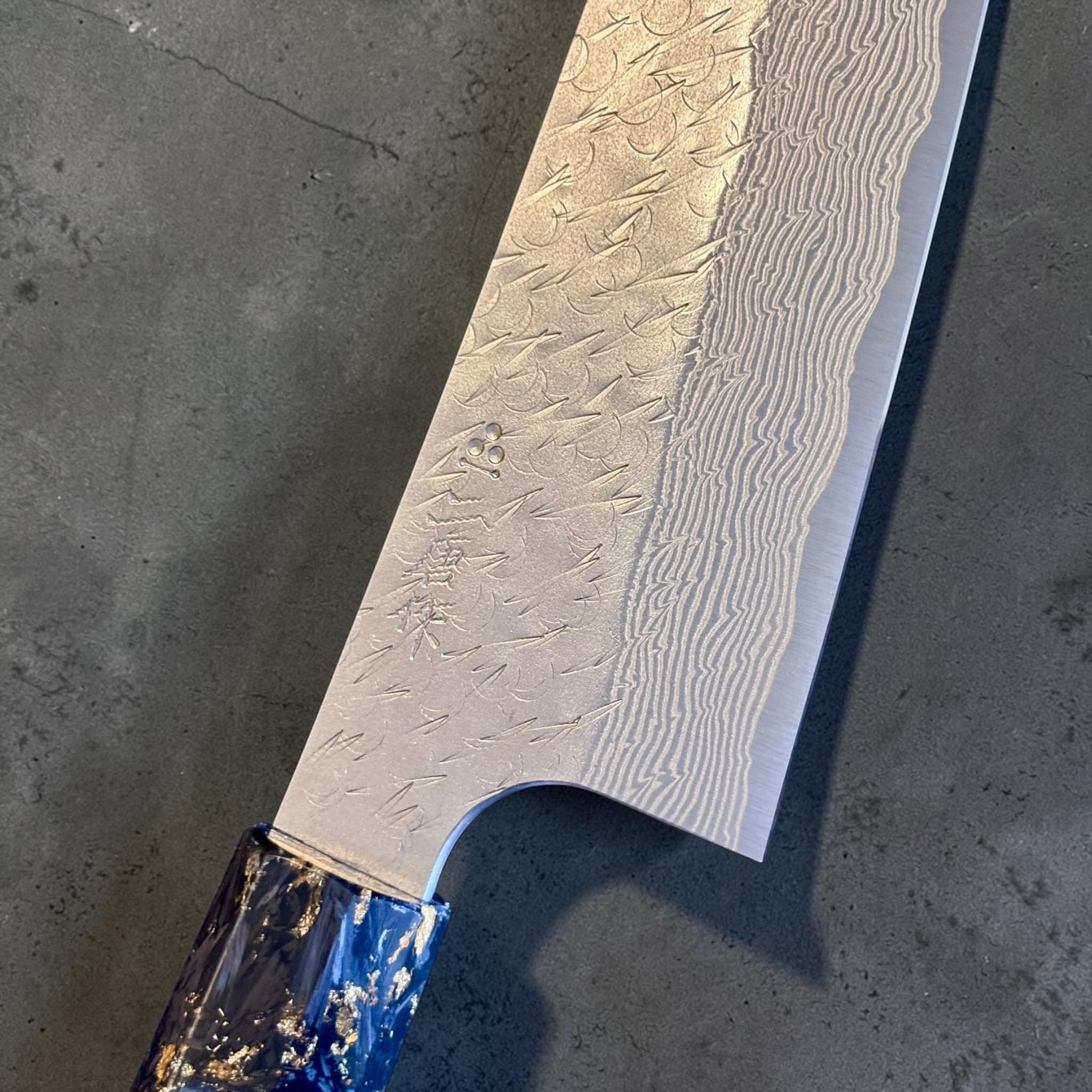 Close-up of the Nigara SG-STRIX Ko Santoku 150 mm blade showing the maker’s mark, intricate Damascus pattern and tsuchime hammered finish.