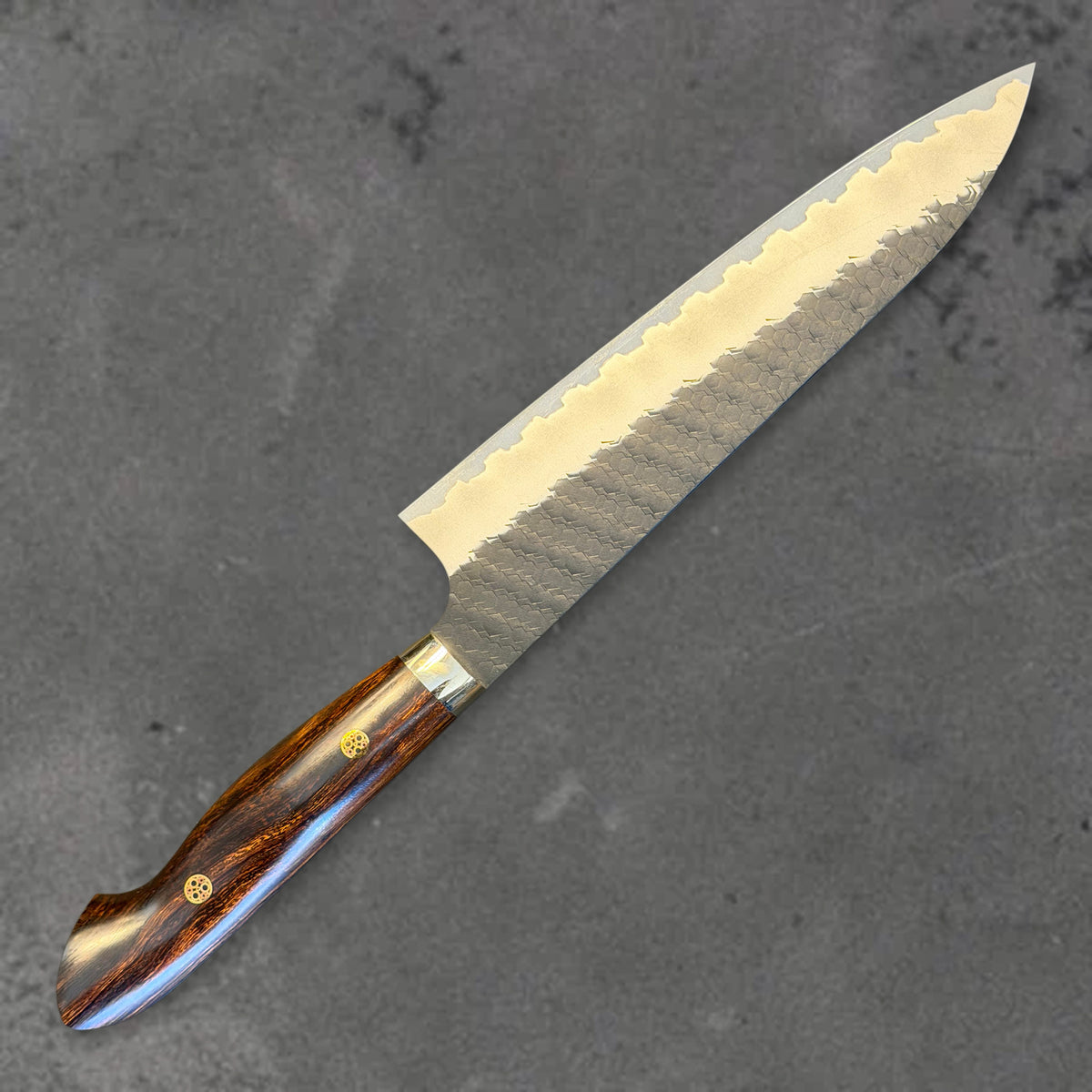 Angled reverse view of the Nigara SG2 Kurouchi Tsuchime 210mm gyuto with ironwood handle, showing the blade shape, finish, and handle.