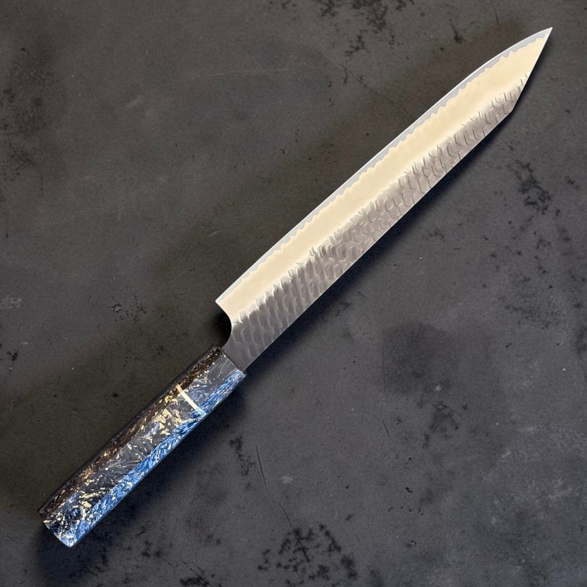 Nigara SG2 Kurouchi Tsuchime Kiritsuke Sujihiki 255 mm, angled view showing hammered SG2 blade and decorative handle.