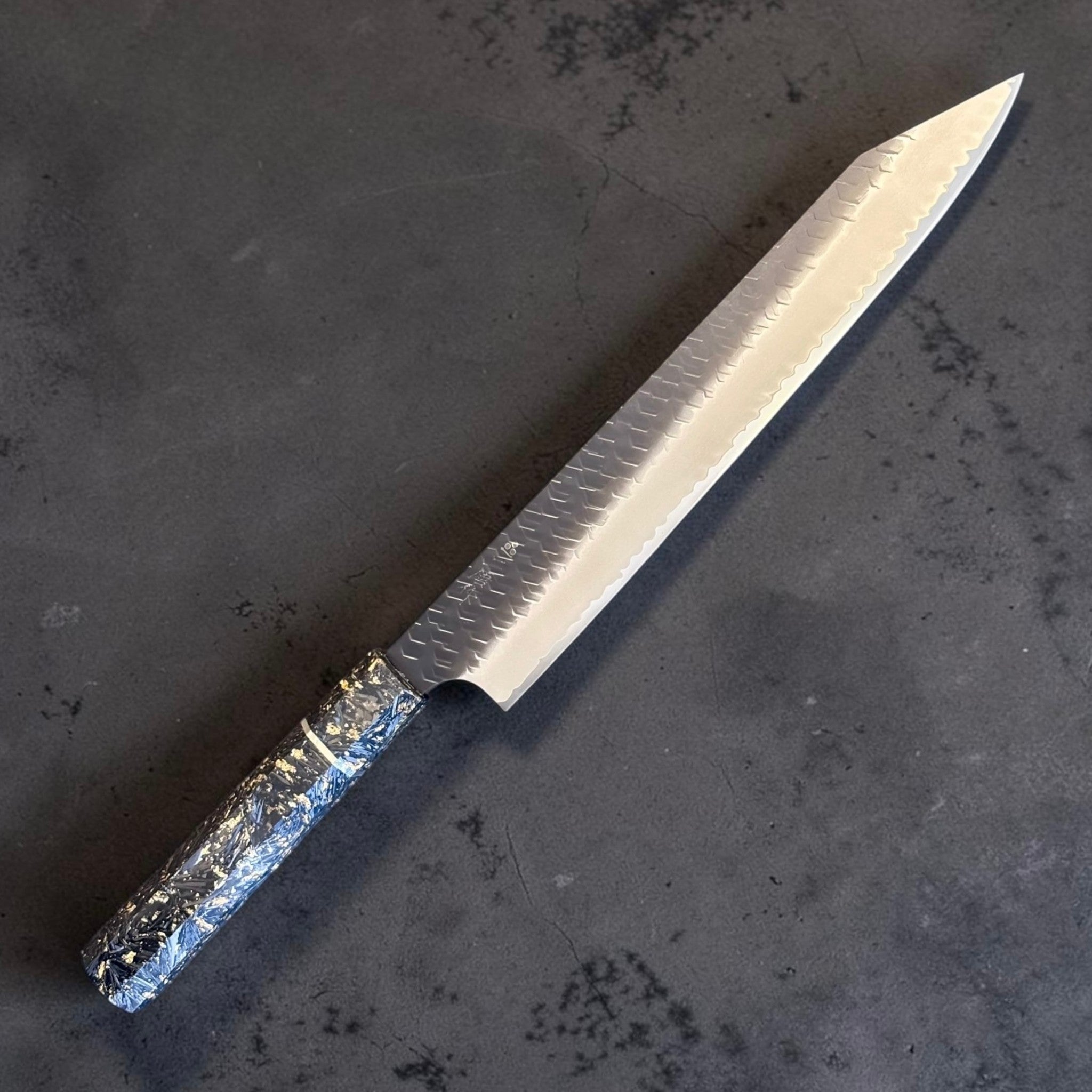 Nigara SG2 Kurouchi Tsuchime Kiritsuke Sujihiki 255 mm, diagonal product view with kurouchi tsuchime finish and gold-accented wa handle.