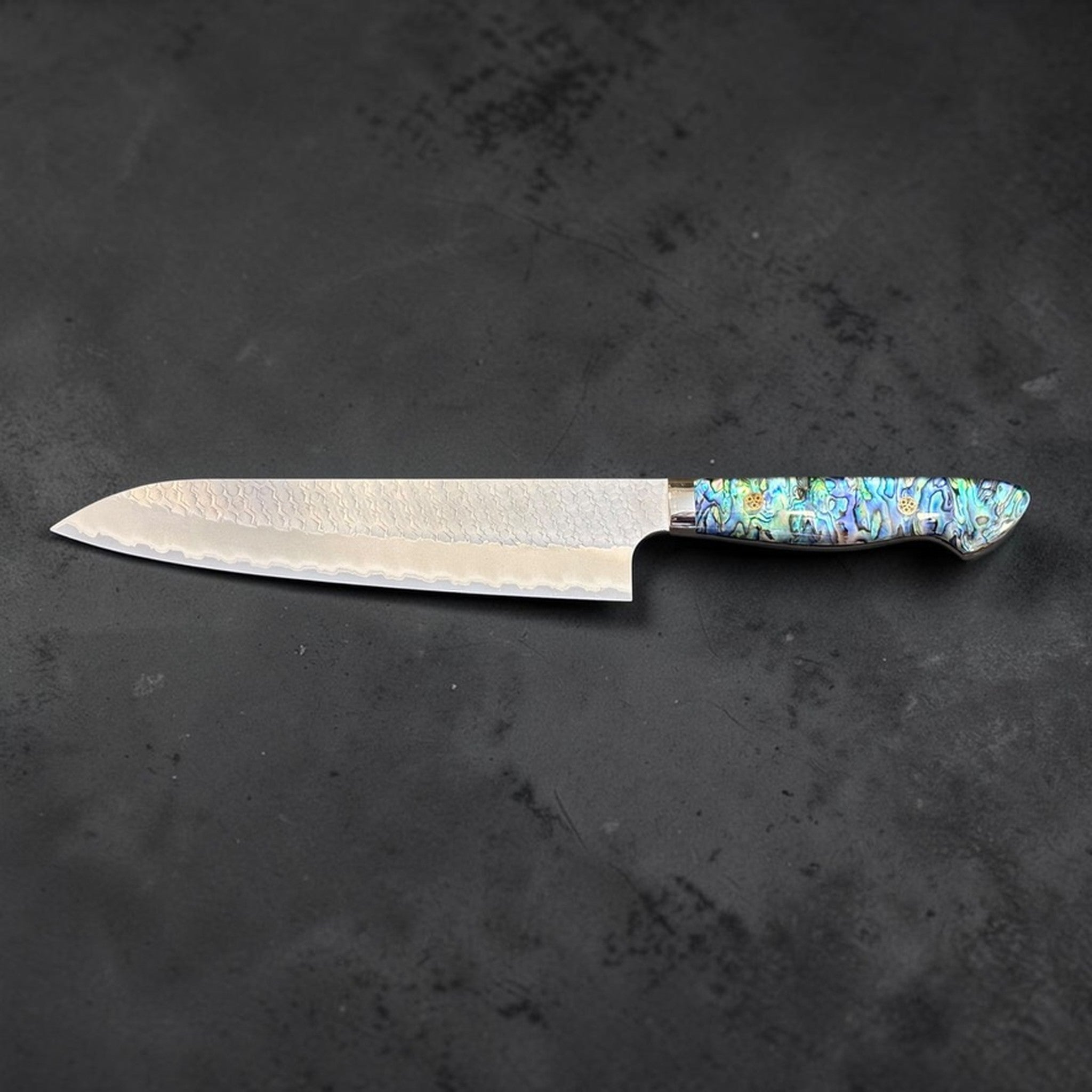 Nigara SG2 Tsuchime Gyuto 240 mm with abalone western handle, full knife left-facing profile on dark stone background.