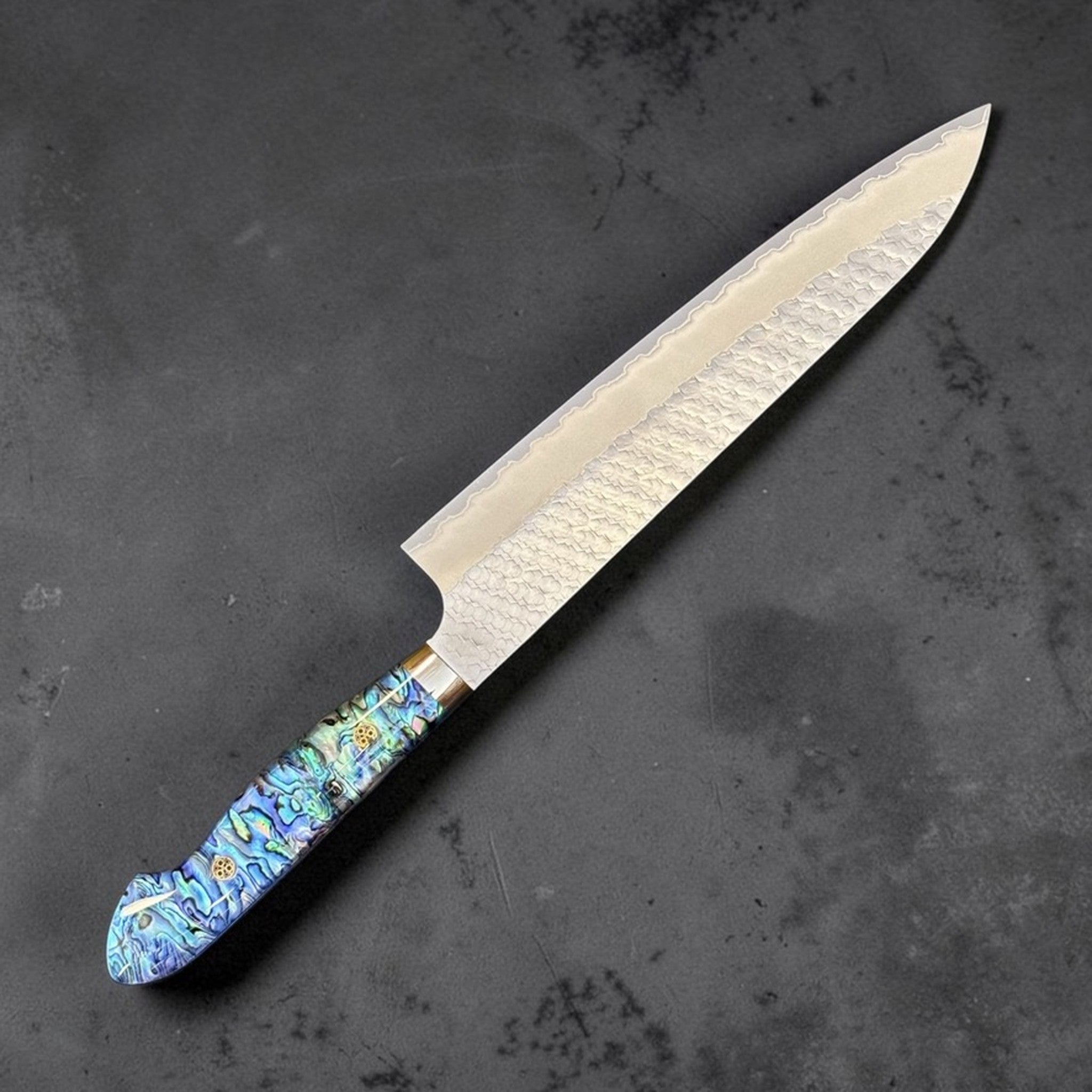 Nigara SG2 Tsuchime Gyuto 240 mm with abalone western handle, angled view showing blade profile and iridescent handle detail.