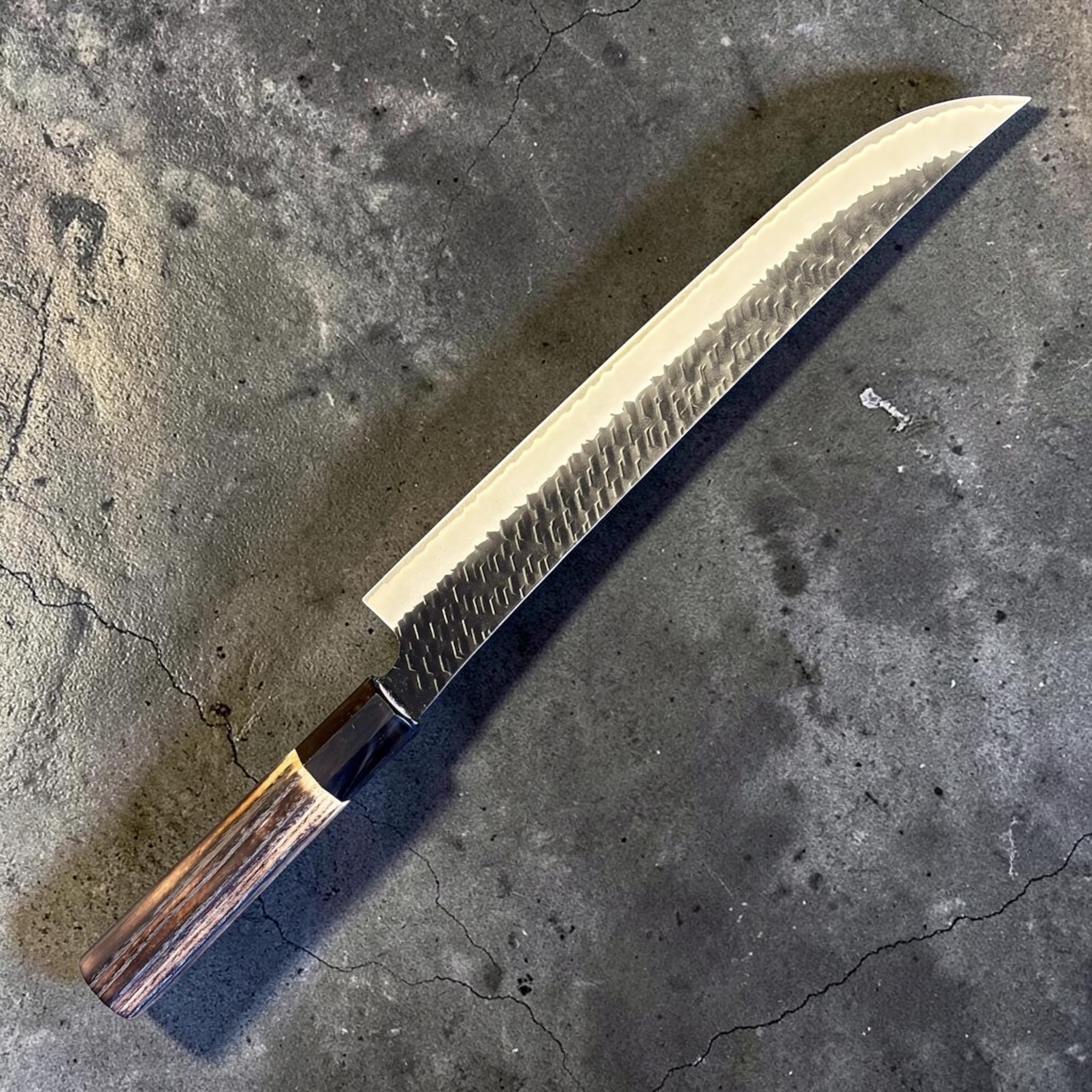 Nigara SG2 Tsuchime Kurouchi Sakimaru Sujihiki 270 mm with wa handle, full angled product view showing the long sakimaru profile and hammered kurouchi blade finish.