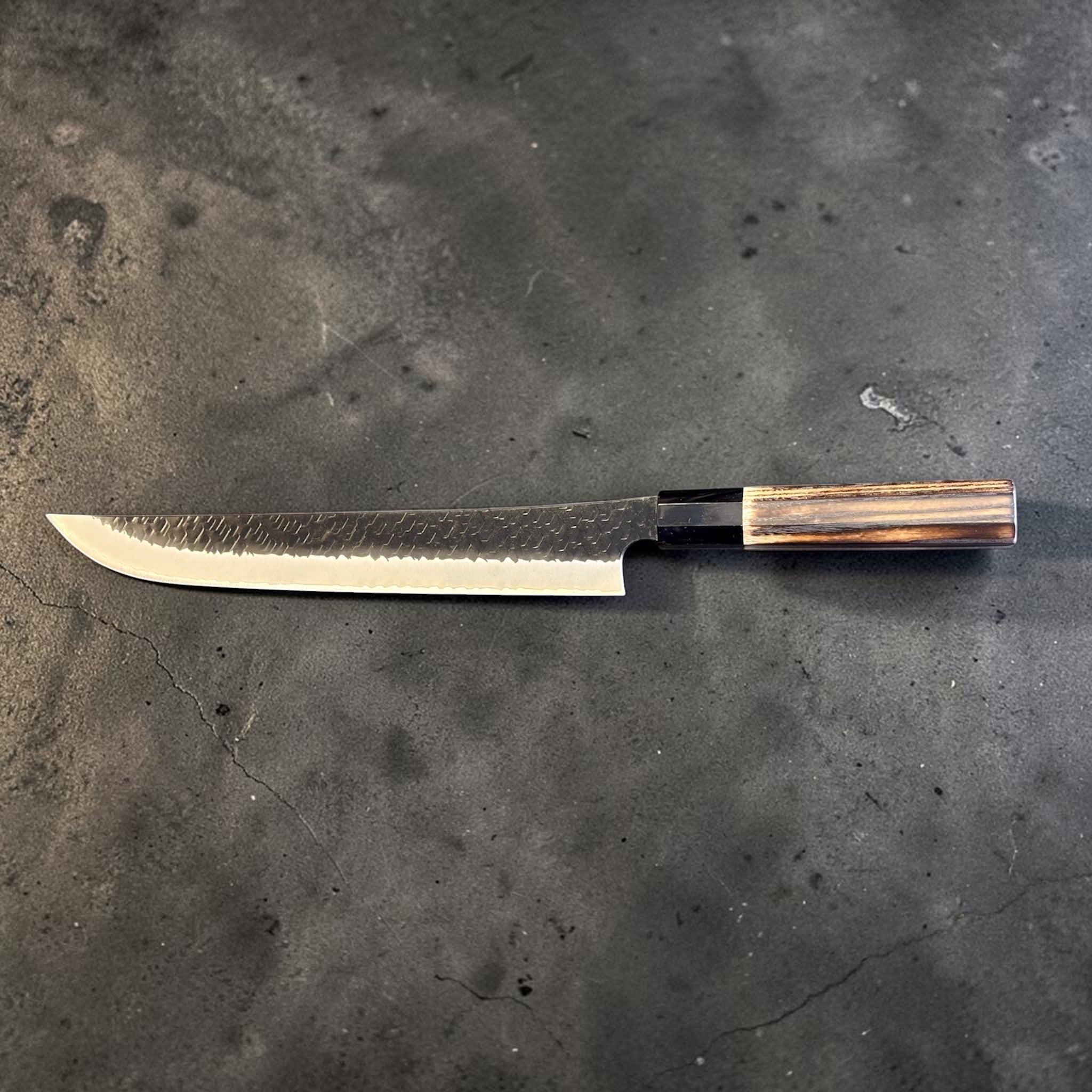 Nigara SG2 Tsuchime Kurouchi Sakimaru Sujihiki 270 mm, full side profile showing the slender slicer blade and contrasting wood wa handle.