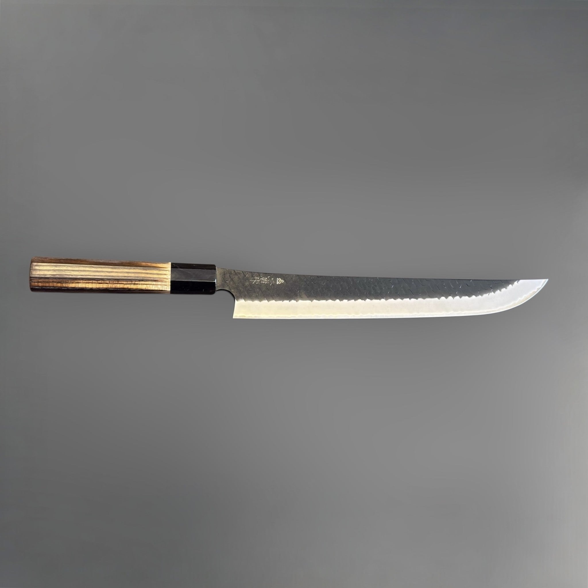 Nigara SG2 Tsuchime Kurouchi Sakimaru Sujihiki 270 mm, reverse side profile with visible kanji, hammered kurouchi texture, and polished bevel.