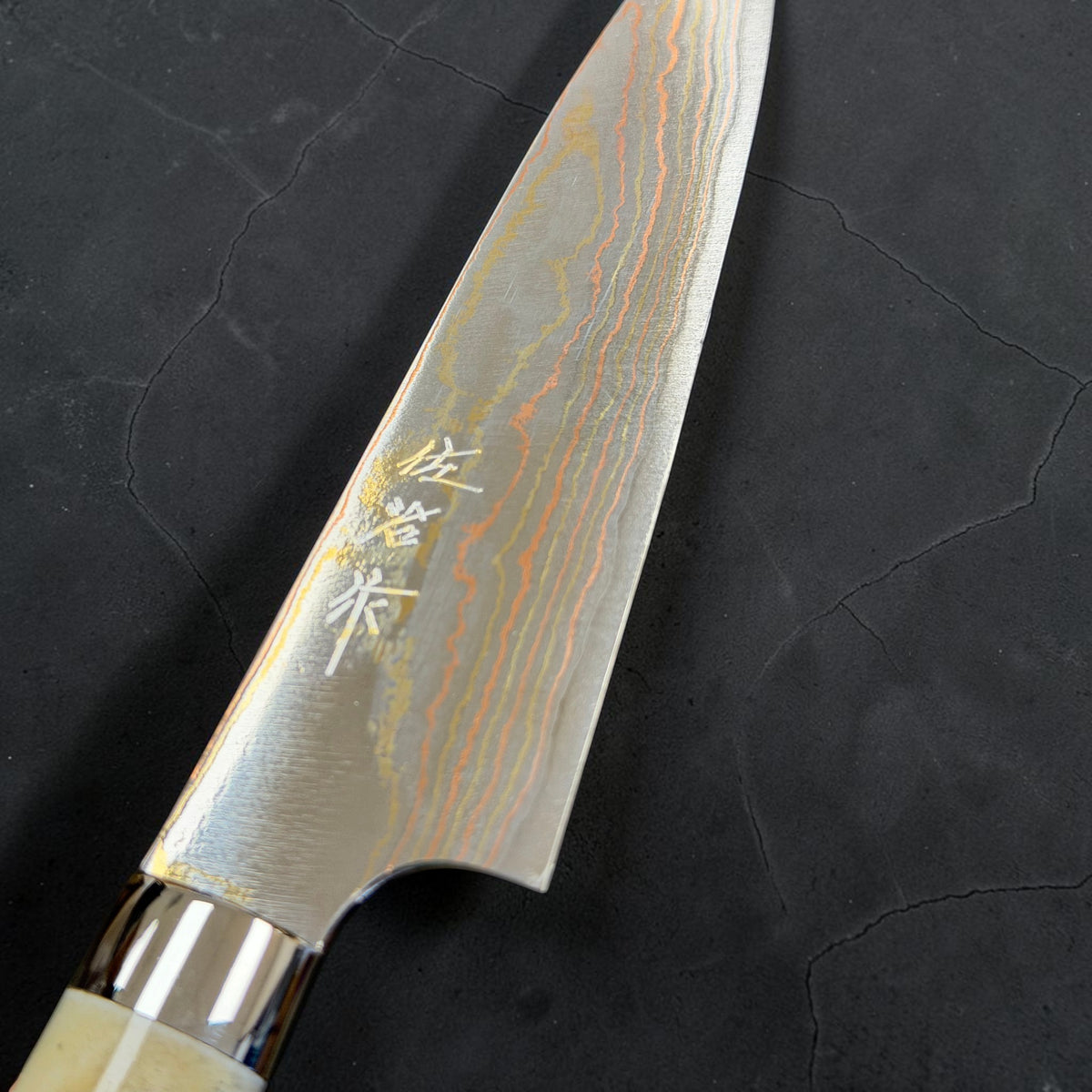 Kanji and rainbow detail of Takeshi Saji Blue #2 Rainbow Damascus Petty 150mm with white cow-horn western handle.