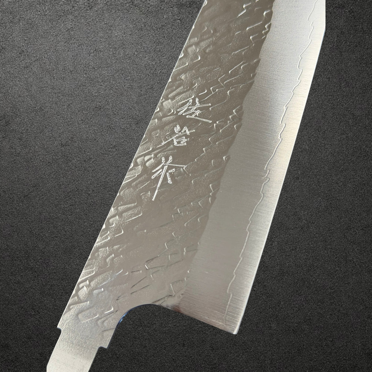 Close-up of engraved Saji kanji, polished tsuchime texture and cladding line on the STRIX santoku blade.