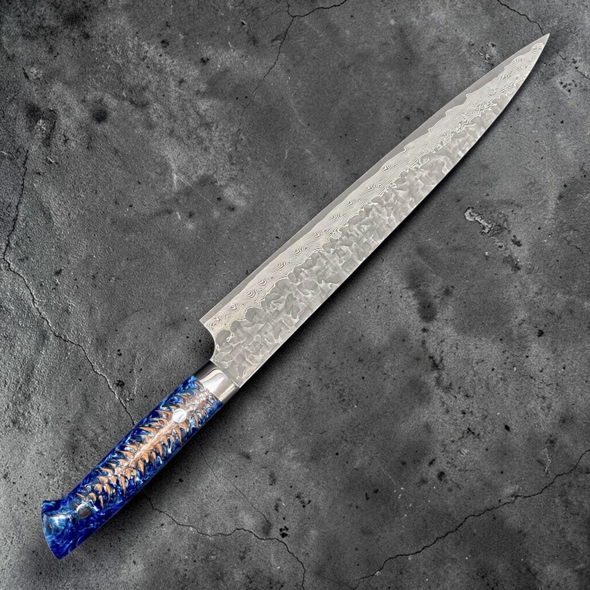 Takeshi Saji VG-10 Kuro Cross Tsuchime Sujihiki 240 mm with pinecone resin western handle, close angled view highlighting the cross tsuchime finish and layered VG-10 Damascus pattern.