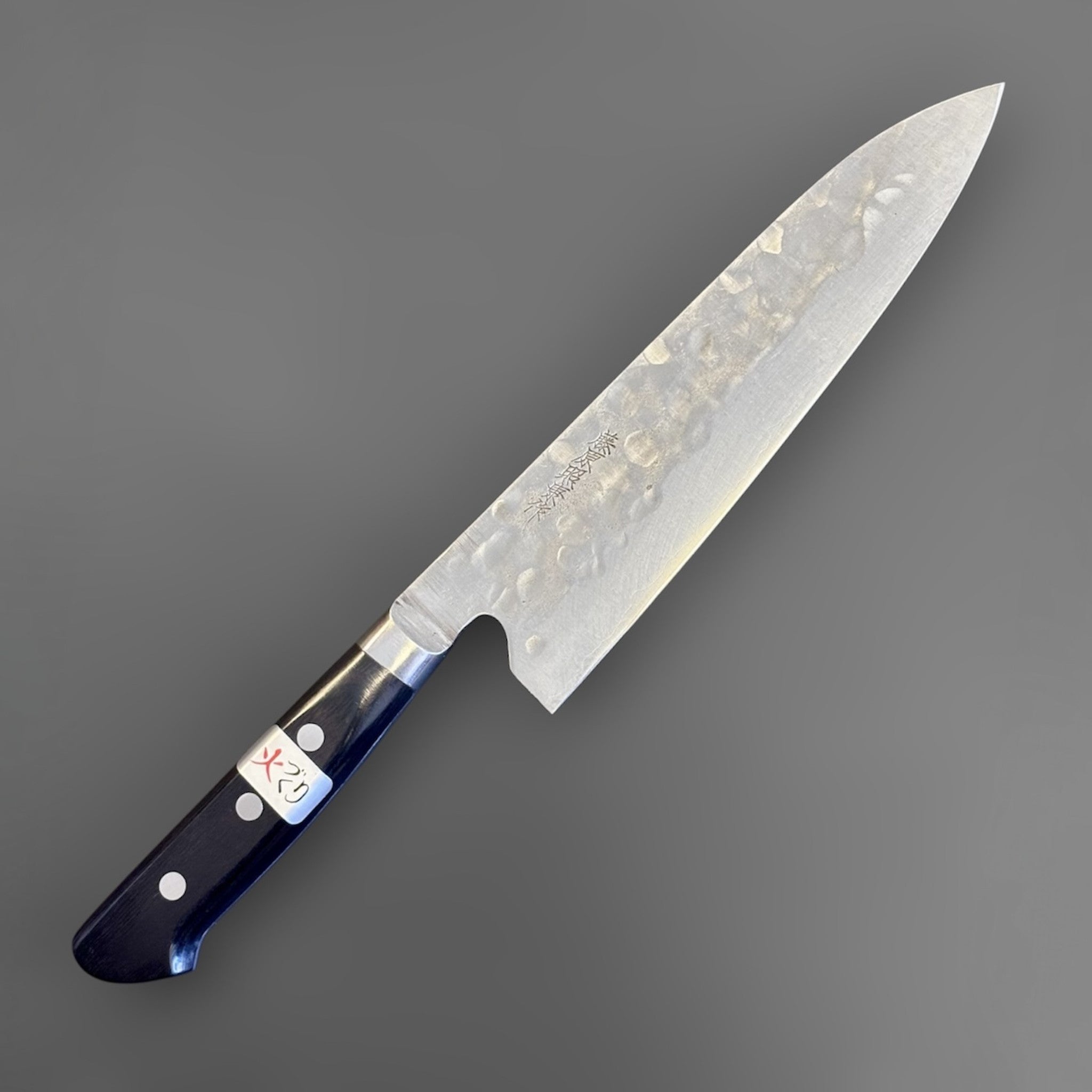 Teruyasu Fujiwara Maboroshi Gyuto 195 mm with western handle, three-quarter front view showing the forged kurouchi-like texture and polished edge.