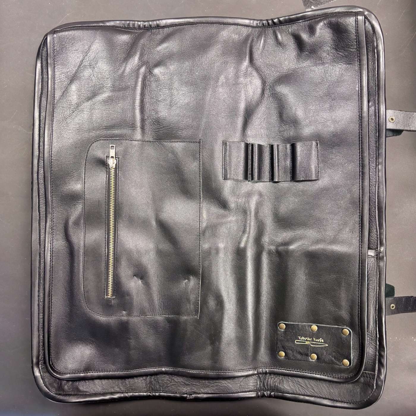 Tokushu Knife Premium Leather Knife Roll interior with zip pocket, elastic tool loops, and brass-riveted Tokushu logo patch