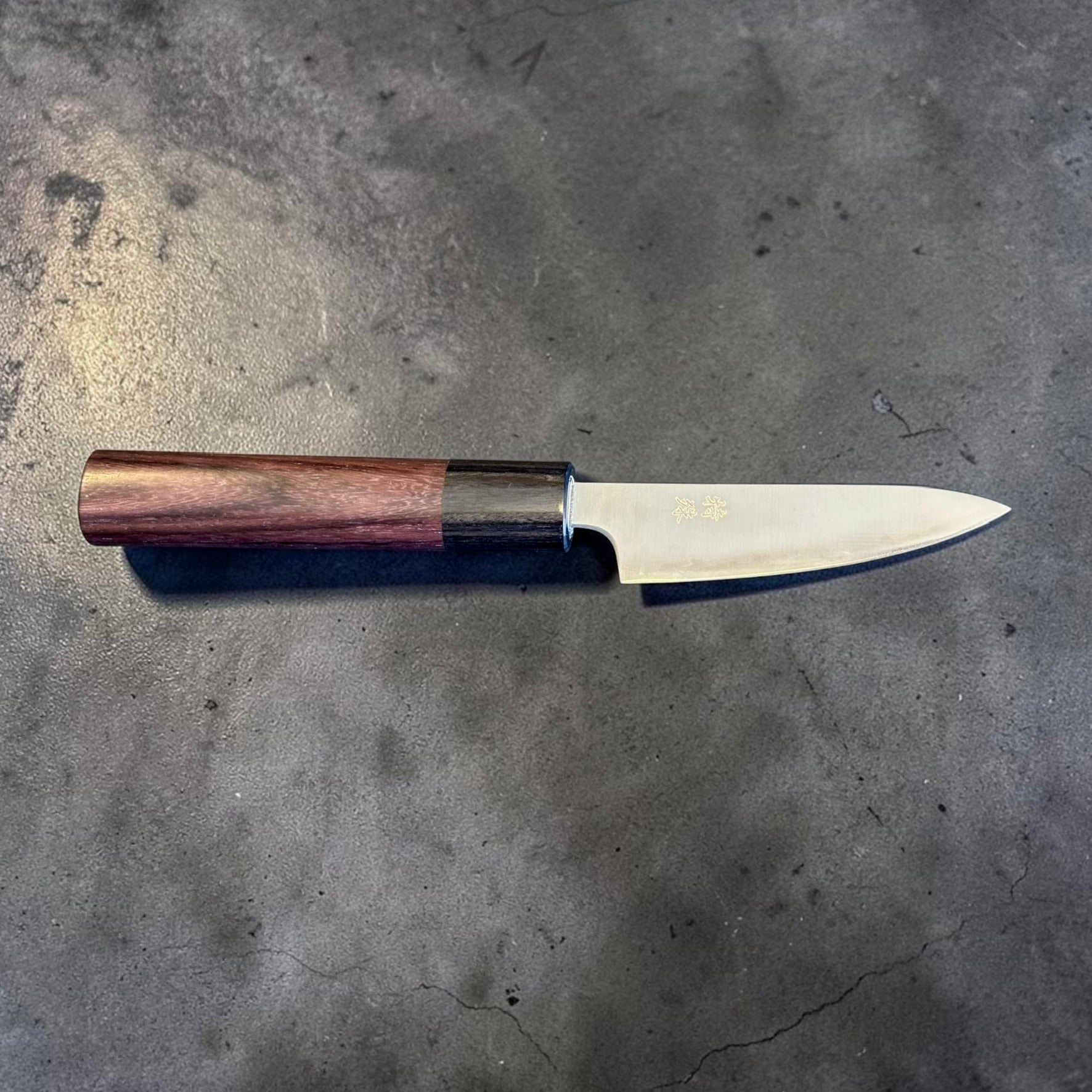 Tokushu Knife Stainless Clad Aogami Super Migaki Petty 80mm, full profile view on dark stone surface.