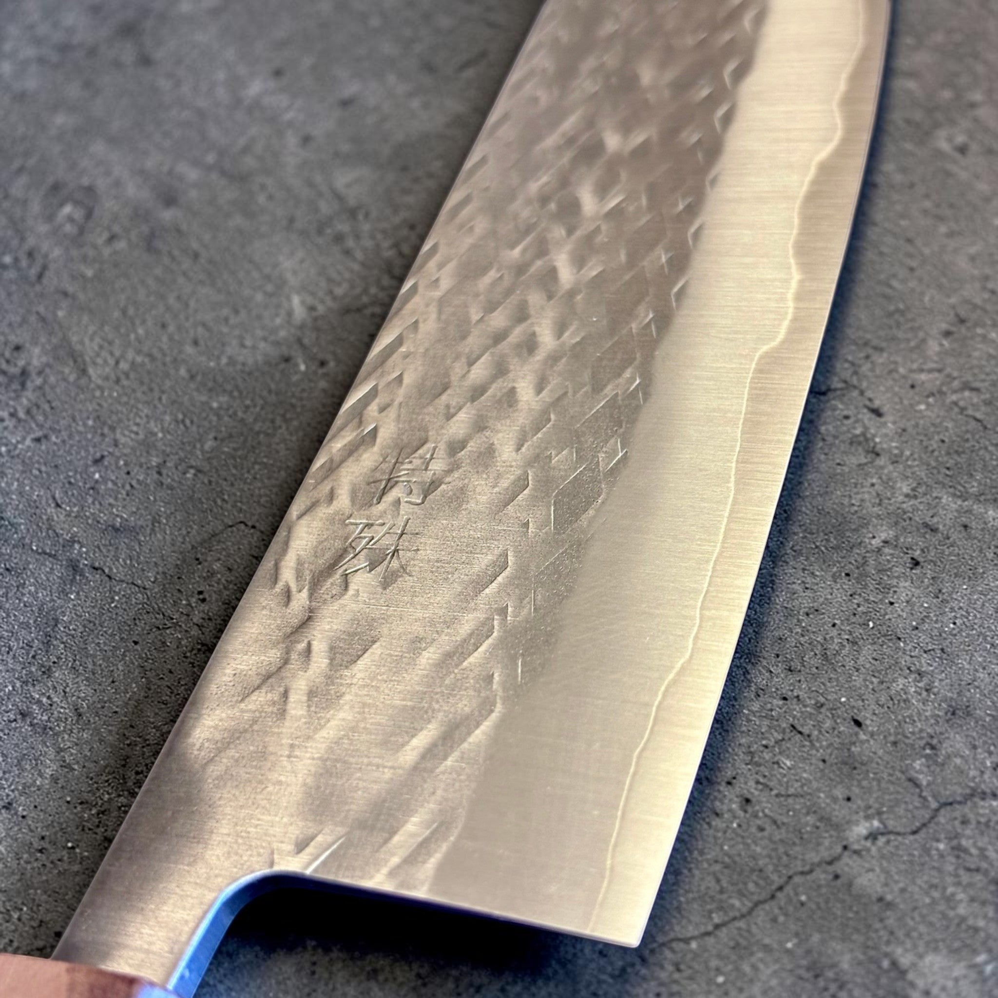 Tokushu Knife Tsuchime SLD Gyuto 240 mm, close-up of the blade face with engraved kanji, tsuchime pattern, and cladding line.