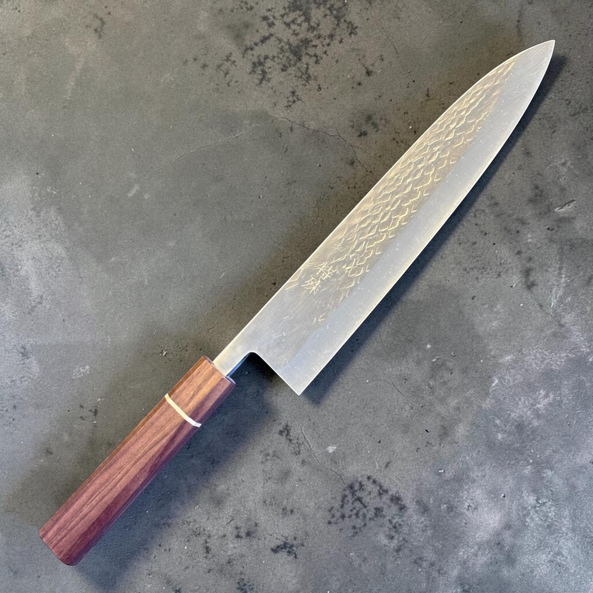 Tokushu Knife Tsuchime SLD Gyuto 240 mm, angled front view highlighting the long gyuto profile, pointed tip, and wood wa handle.
