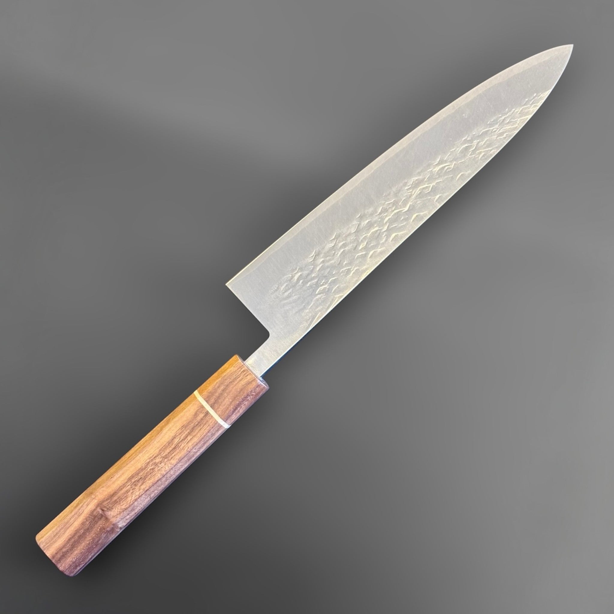 Tokushu Knife Tsuchime SLD Gyuto 210 mm, angled front view showing the hammered tsuchime blade finish and warm wood wa handle.