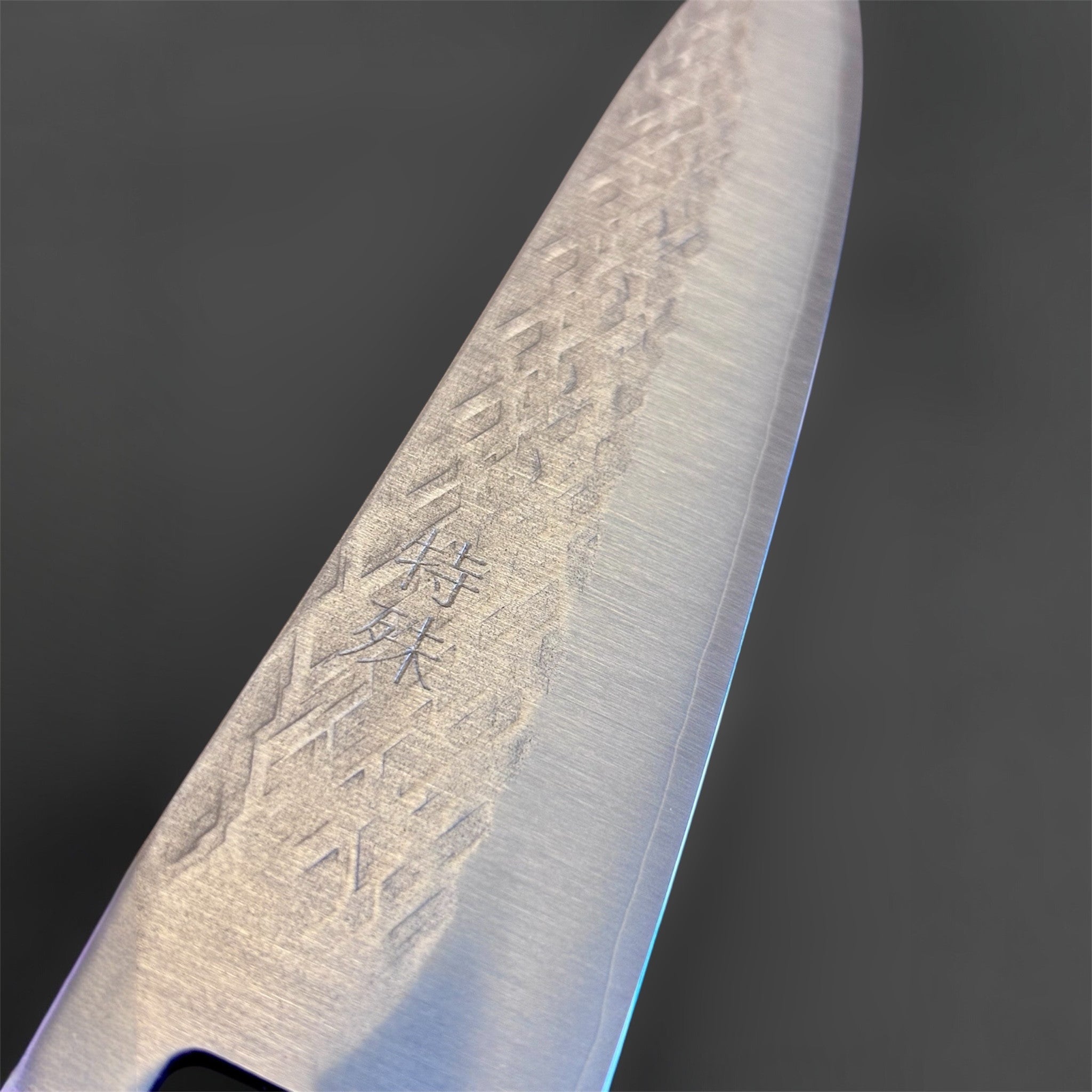 Tokushu Knife Tsuchime SLD Gyuto 210 mm, close-up detail of the blade face with engraved kanji and hammered tsuchime pattern.