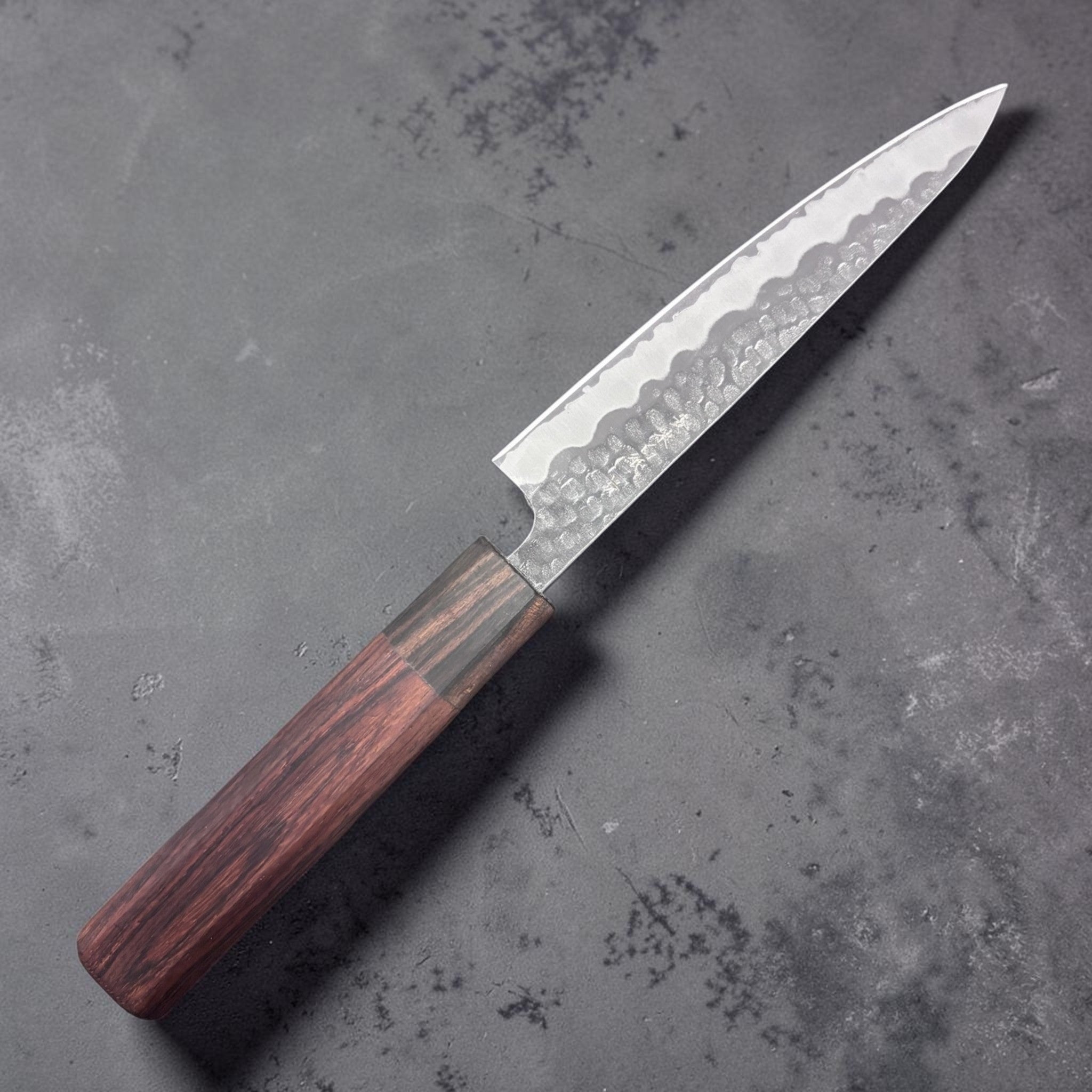 Tokushu Tsuchime White #2 Petty 135 mm with rosewood wa handle, front-left side profile of blade showing hammered cladding
