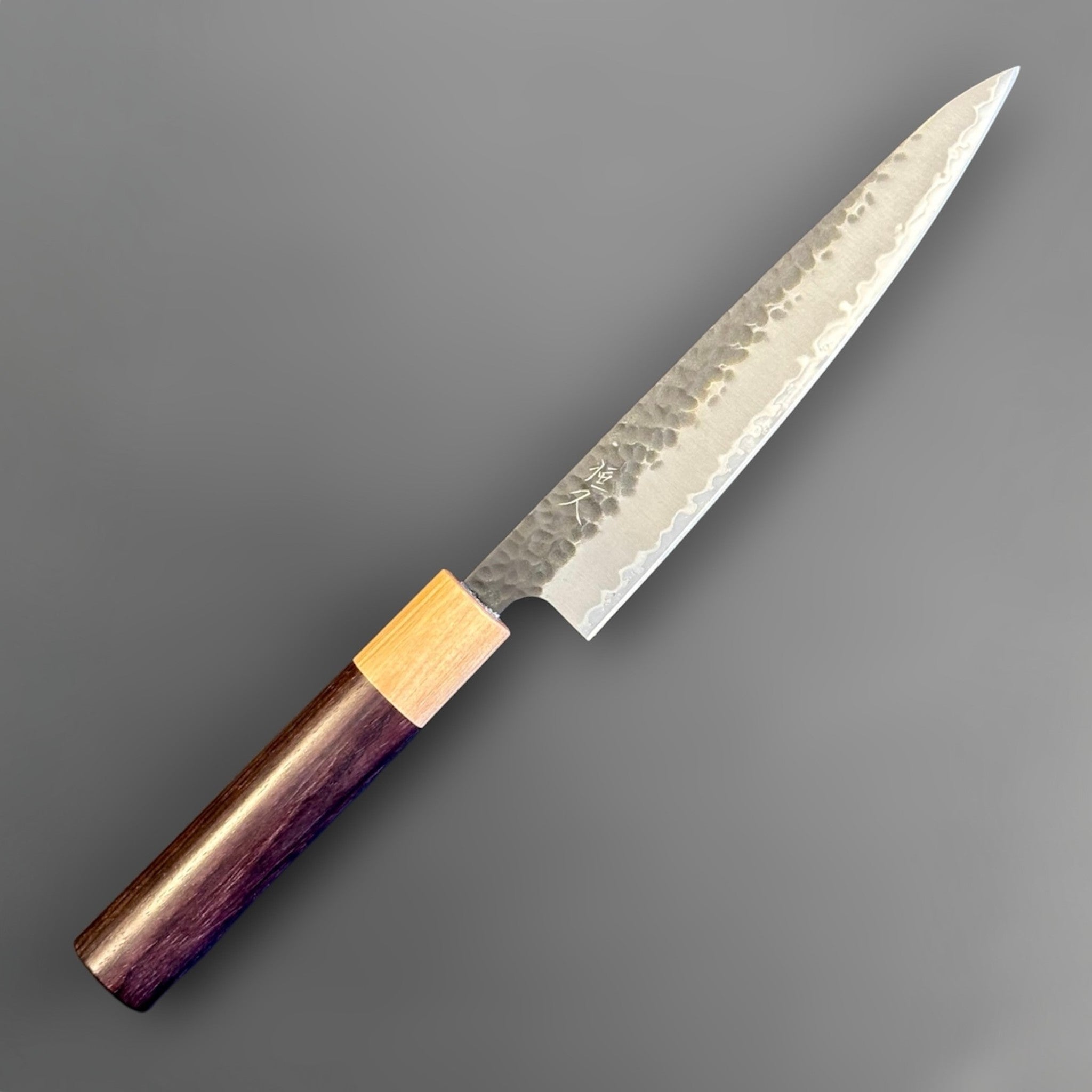 Tsunehisa Aogami Super Tsuchime Kuro Petty 150 mm with morado handle, angled front-side view showing the kurouchi finish, hammered tsuchime texture, and polished core steel edge.