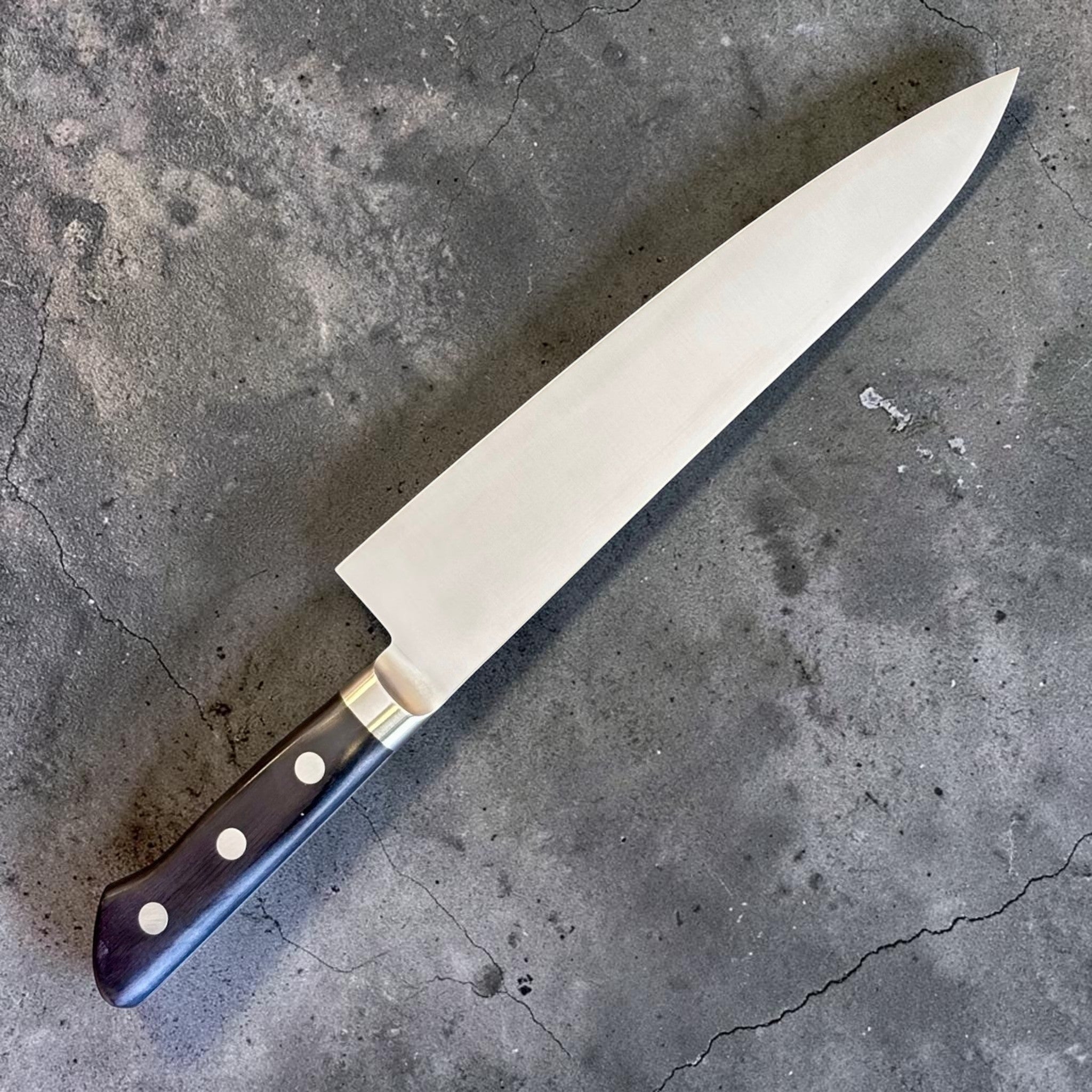 Tsunehisa Mono AUS-8 Gyuto 210 mm with black Western handle, angled full knife view showing the opposite blade face and black Western handle.