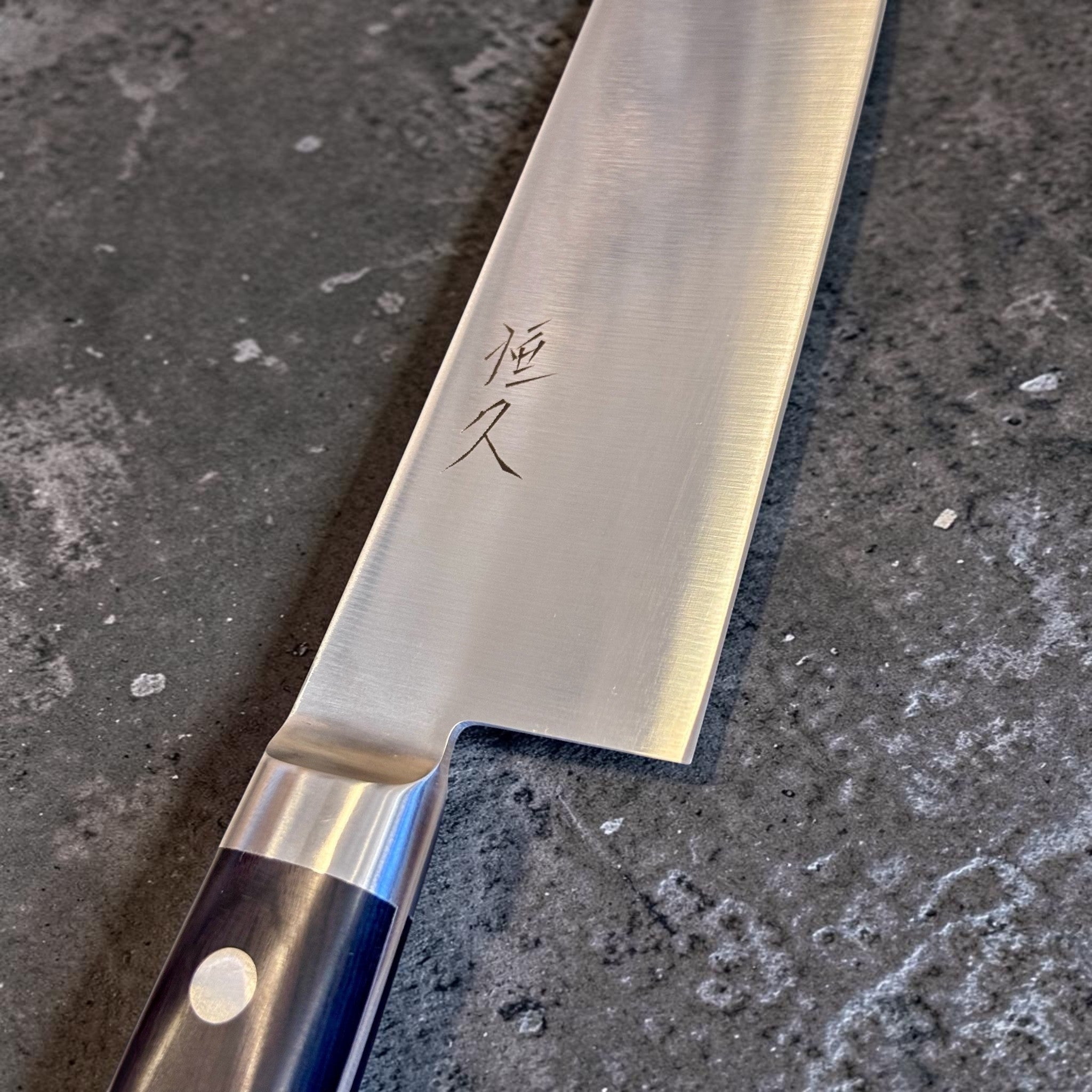 Tsunehisa Mono AUS-8 Gyuto 240 mm with black Western handle, close-up of kanji and brushed AUS-8 blade finish.