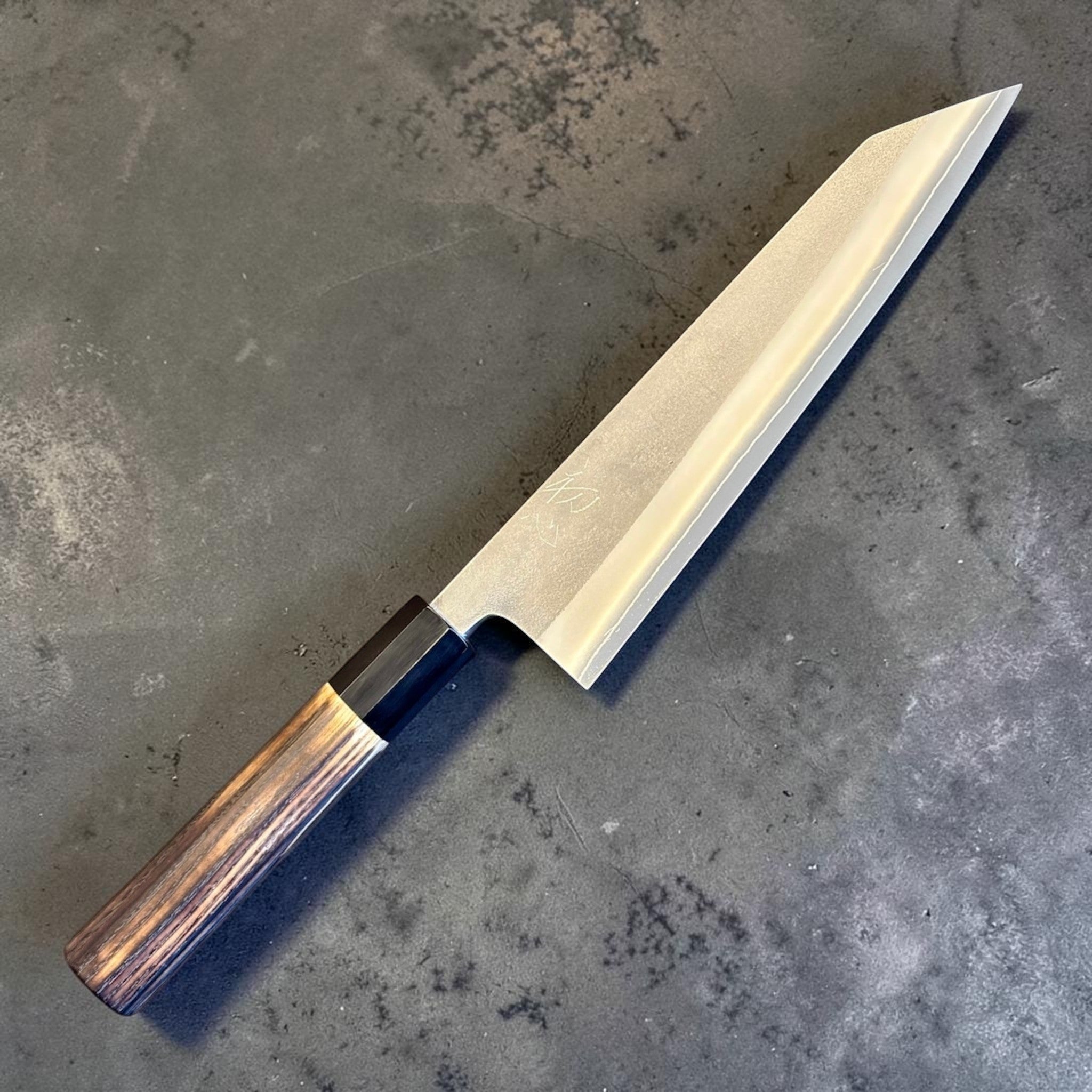 Yoshikane SKD Nashiji Kiritsuke 210 mm with burnt wood and black buffalo horn handle, angled front view on gray background.