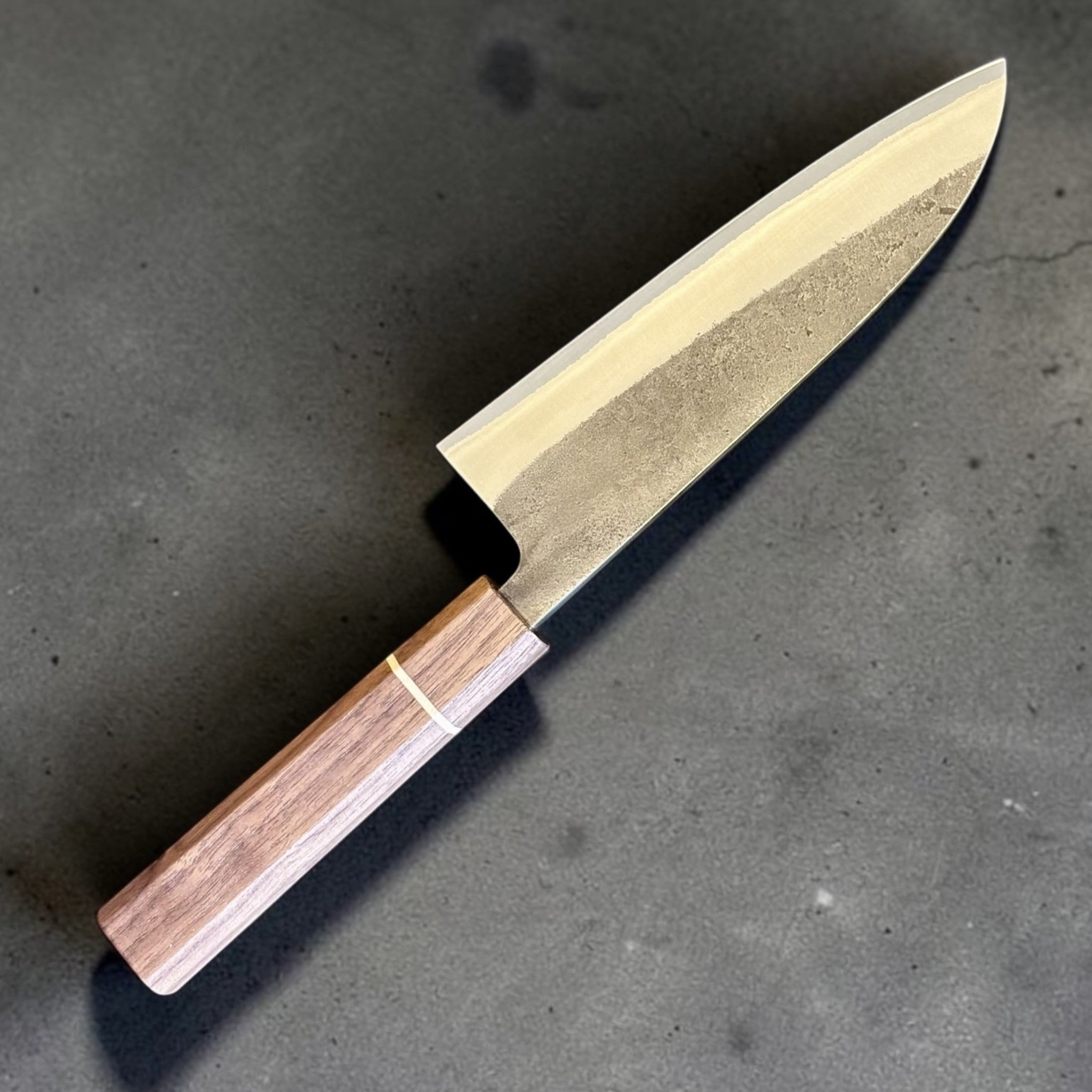 Yoshikane Nashiji Kurouchi Santoku with Sanjo walnut handle, angled full-knife product view showing the textured blade finish.