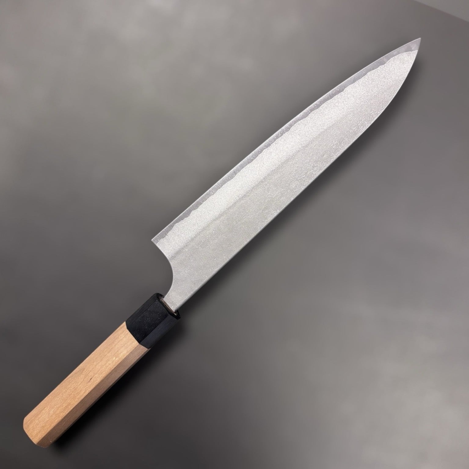 Yoshimi Kato AS Nashiji Gyuto 240mm, angled shot highlighting edge geometry and forged Nashiji pattern.