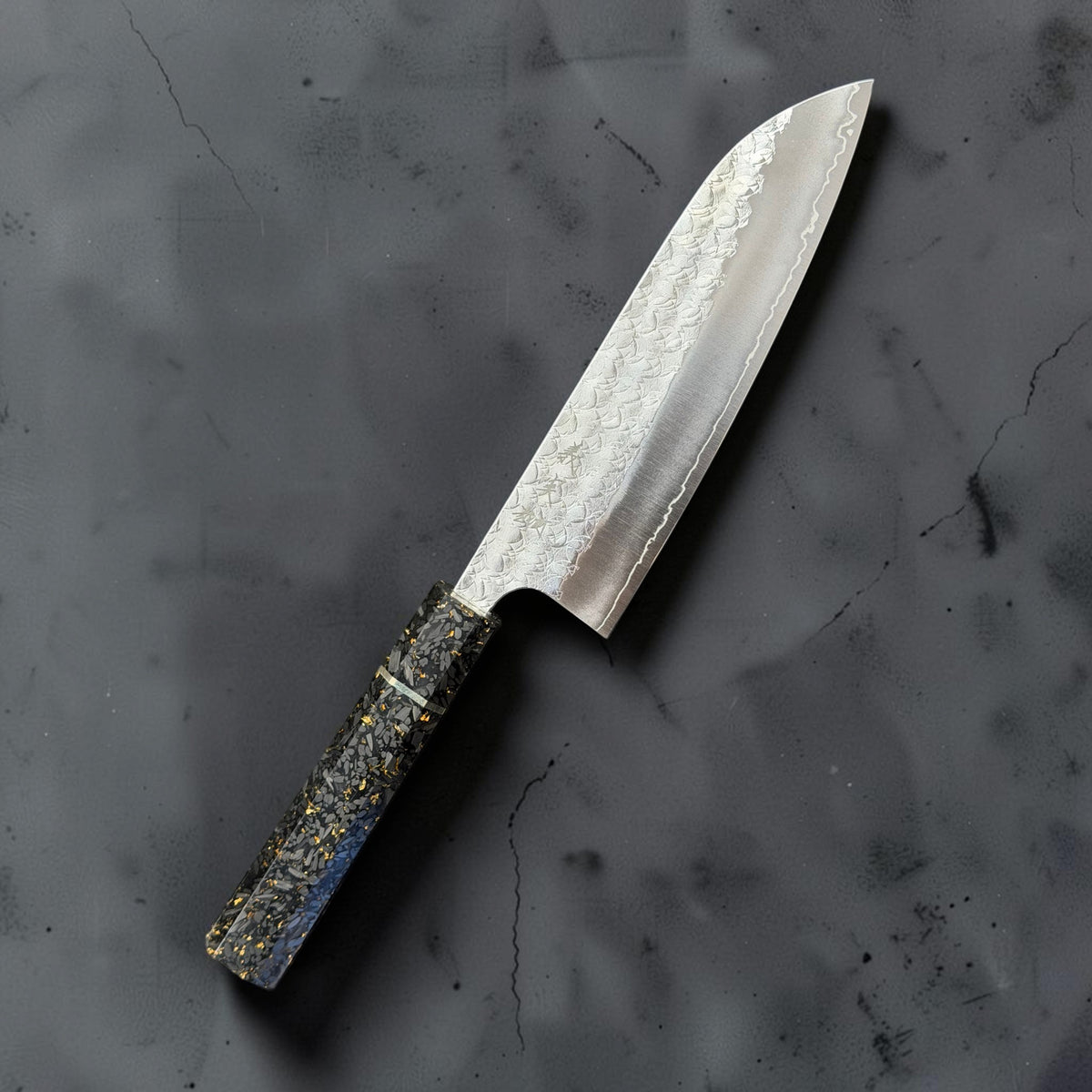 Yoshimi Kato Minamo SG2 santoku with a carbon fiber gold-fleck octagonal handle, angled front view on a dark grey background.