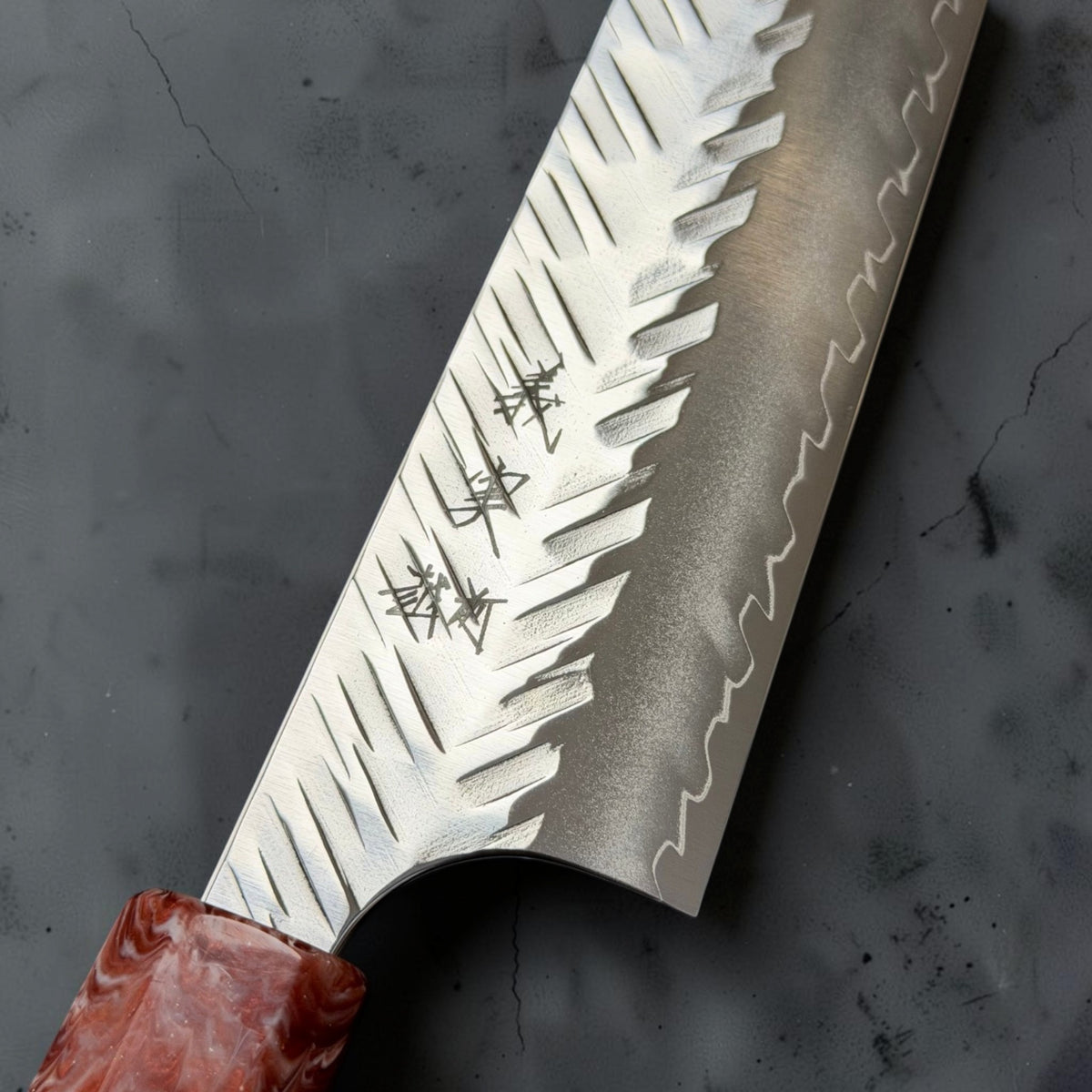 Close-up of Yoshimi Kato SG-STRIX sujihiki showing the V-shaped hammered texture, engraved kanji and wavy cladding line.