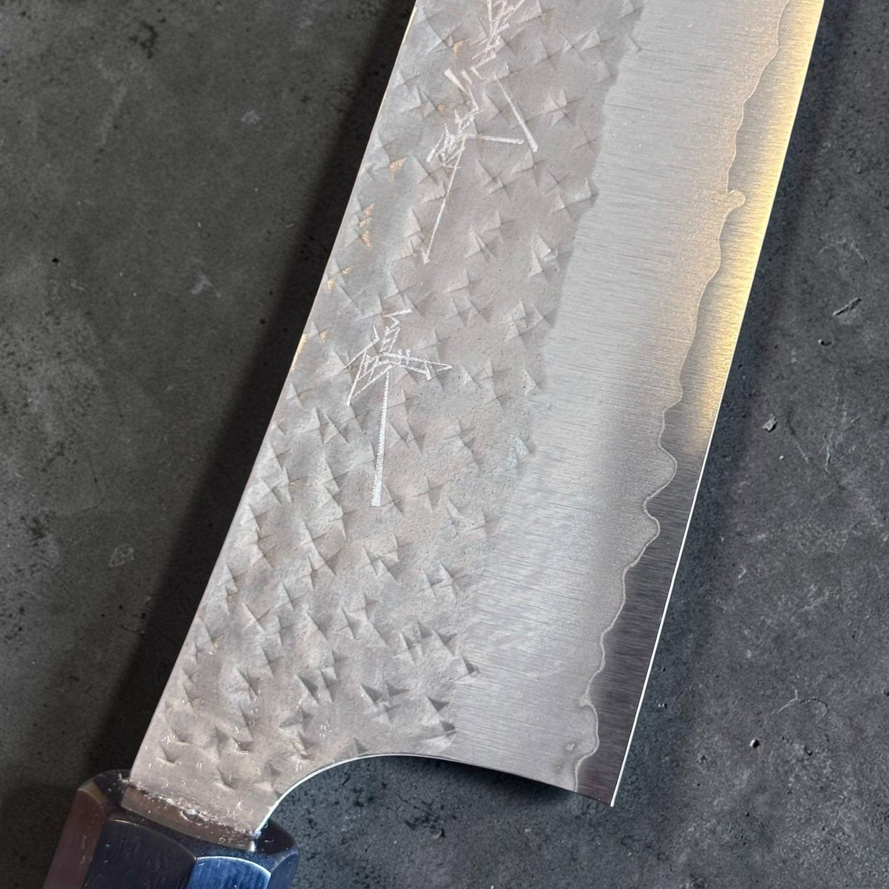 Close-up of the Yu Kurosaki Kokusen AS Gyuto 210mm hammered blade finish, cladding line and maker engraving