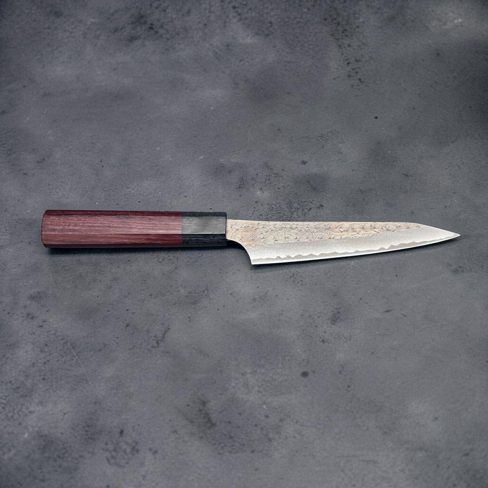 Yu Kurosaki Kokusen AS Petty 120 mm with rosewood octagon wa handle, full side profile on gray background.