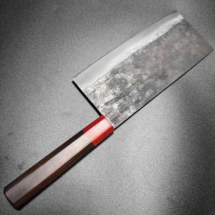 Close-up of the DAO VUA V3 52100 Chinese Cleaver's blade and red handle on a wooden table