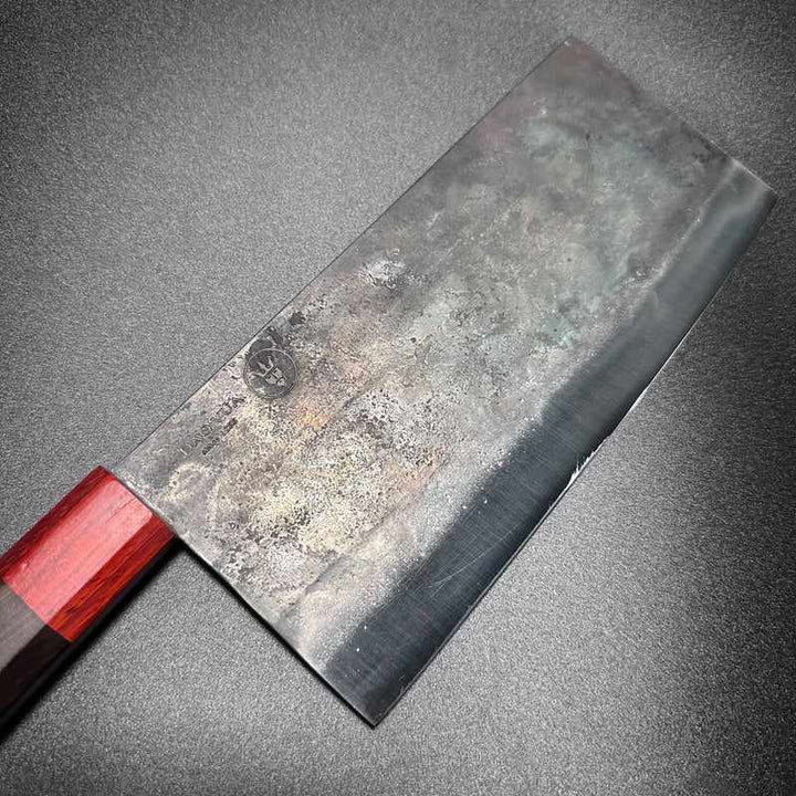 Angled view of the DAO VUA V3 52100 Chinese Cleaver showcasing the blade's edge and red handle on a light surface