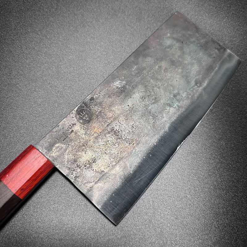 Angled view of the DAO VUA V3 52100 Chinese Cleaver showcasing the blade's edge and red handle on a light surface